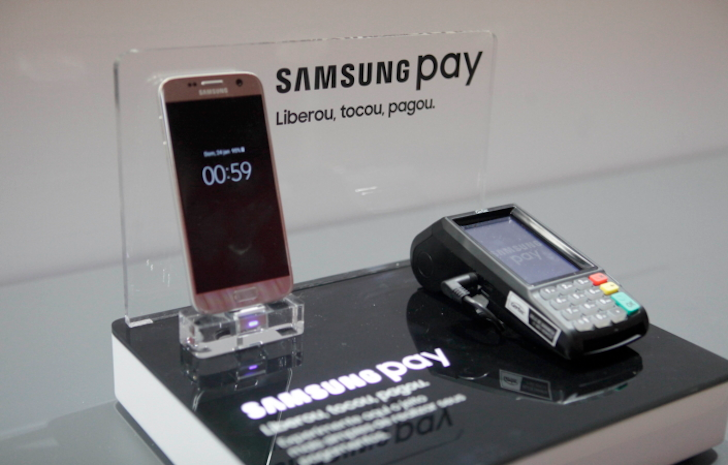 A imagem mostra um display técnico com um telefone Samsung ao lado de um leitor de cartão de pagamento.  O visor diz 