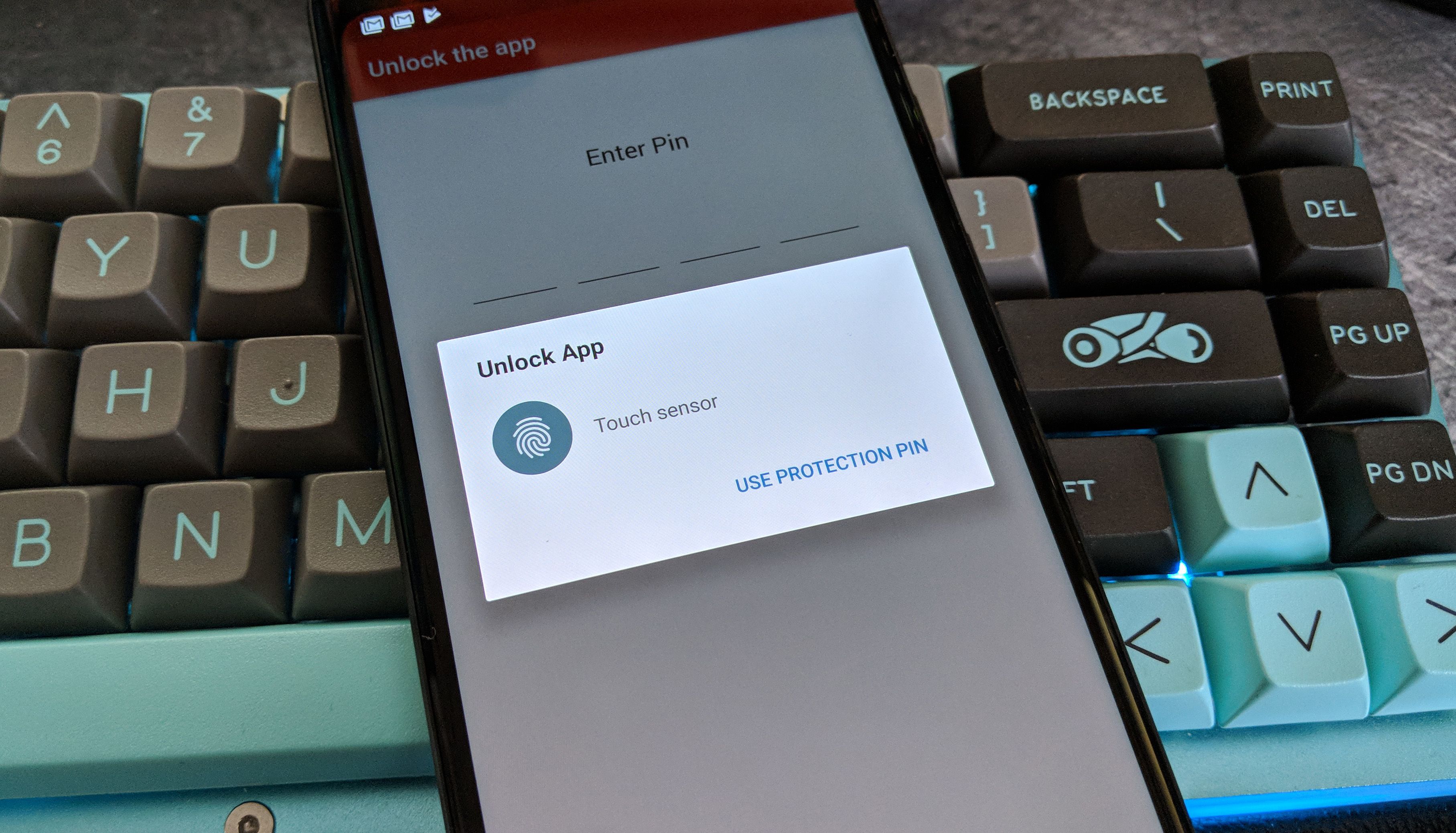 A phone sits on a mechanical keyboard. The Authy app is open on the phone's display. 