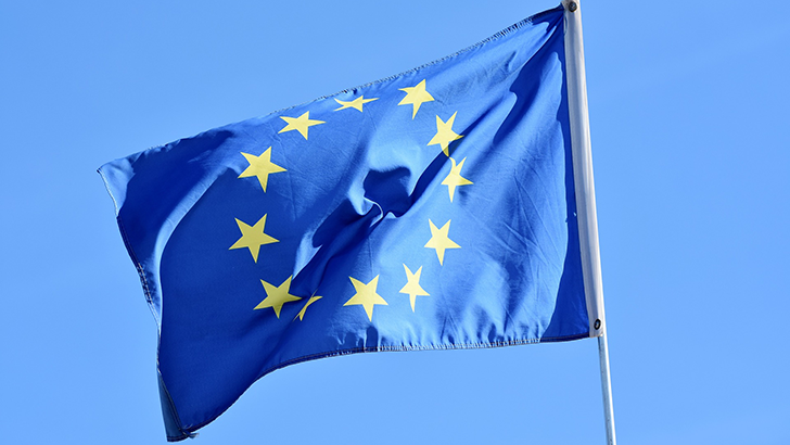 The European Union flag against a blue background fluttering in the wind.