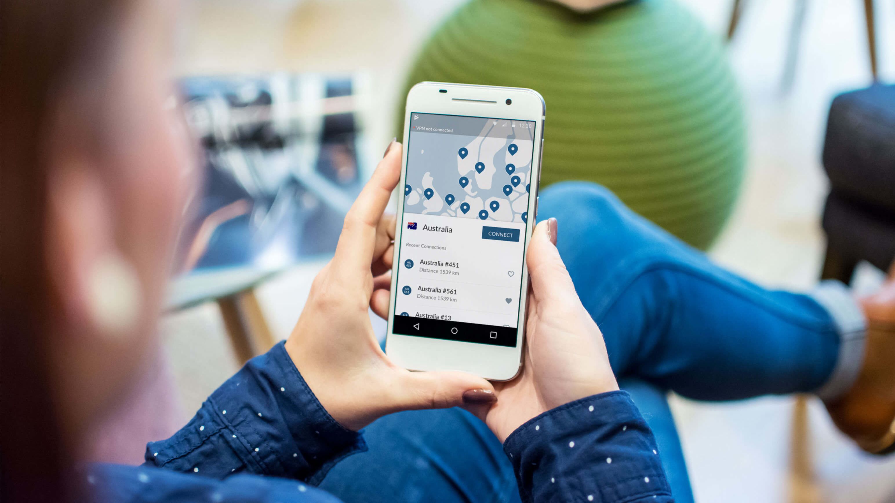 A person in a blue shirt and denim holds a phone with a VPN app open. 