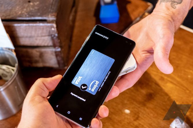 Hand holding Samsung phone with Samsung Pay open at an NFC terminal.