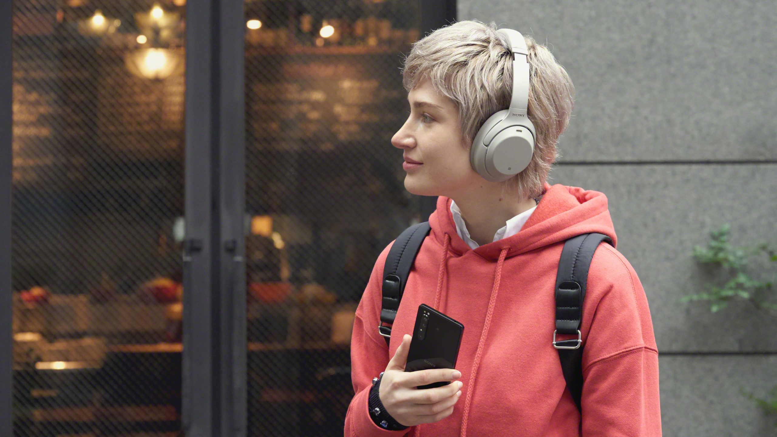A person holding a phone and wearing wireless headphones looks into a cafe window.