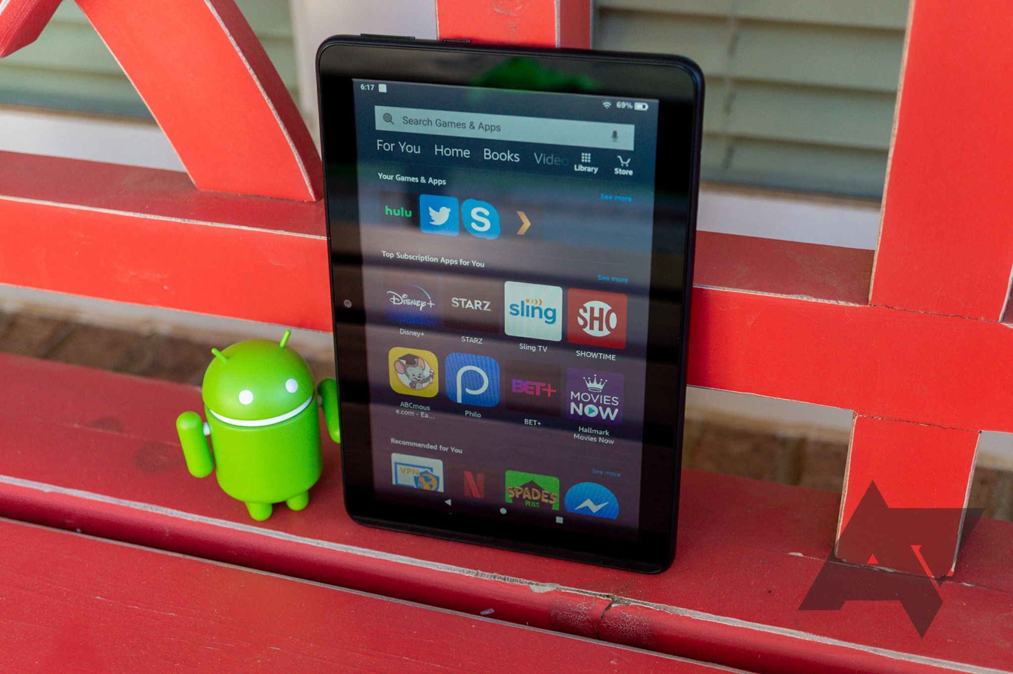 Amazon Fire tablet on a red bench, next to a green Android figurine  