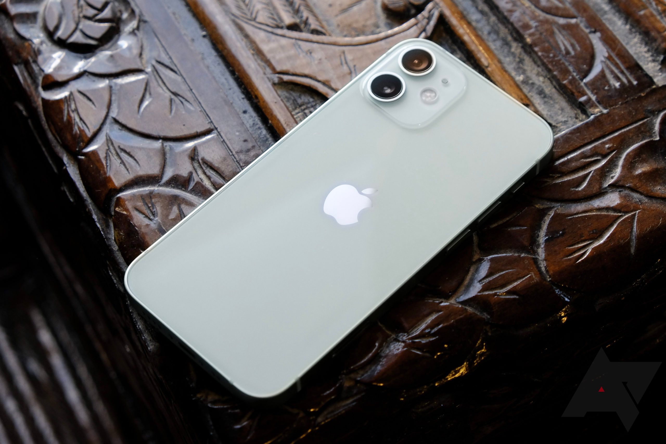 An iPhone 12 mini sits on a carved and lacquered wood surface.