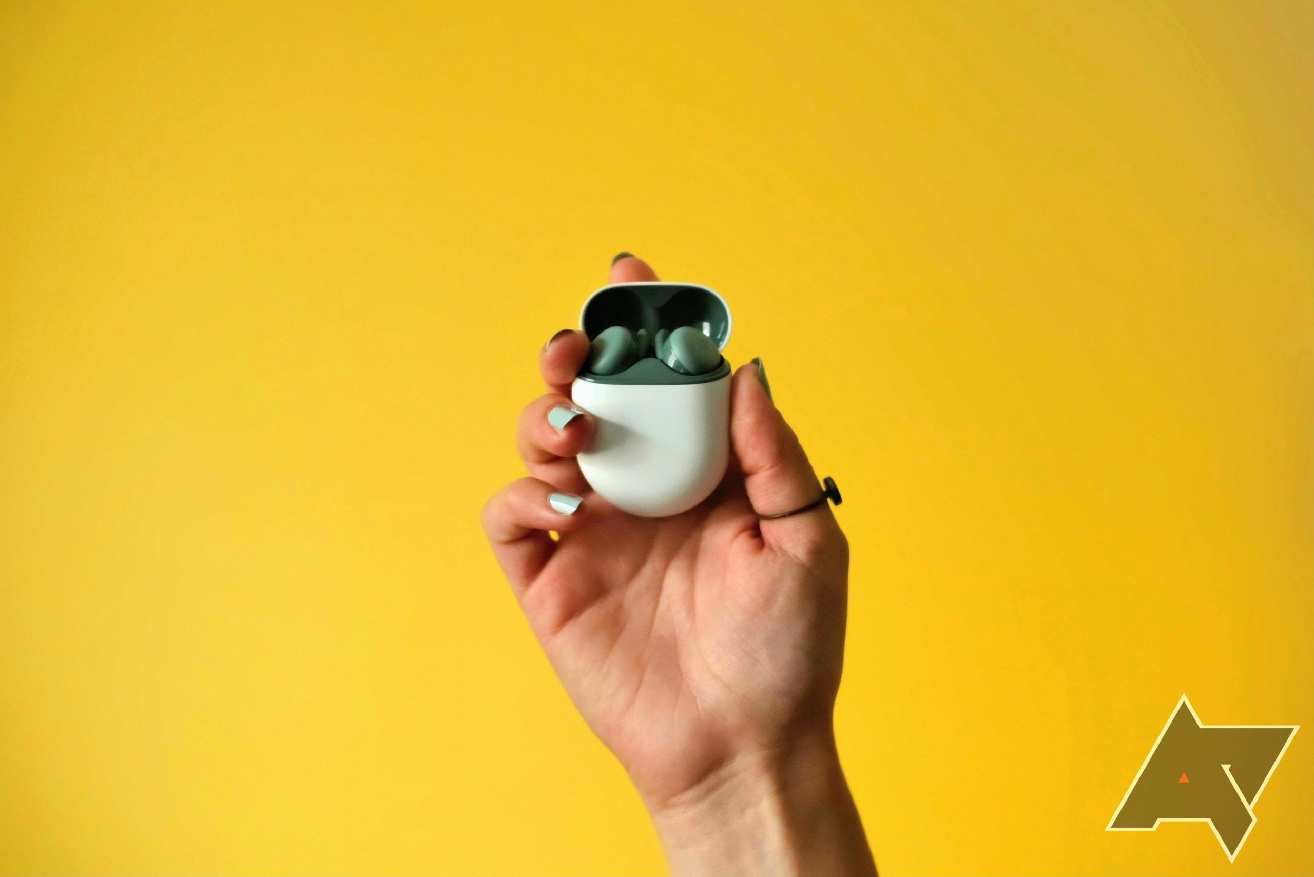 A pair of Google Pixel Buds A series earbud in a case being held by a hand