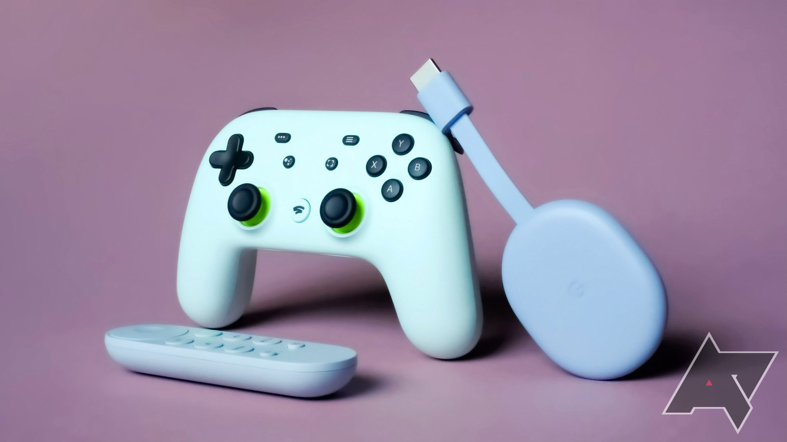 A Google Stadia controller with a Google Chromecast with Google TV leaning on it and the Chromecast remote in front of it with a purple background.