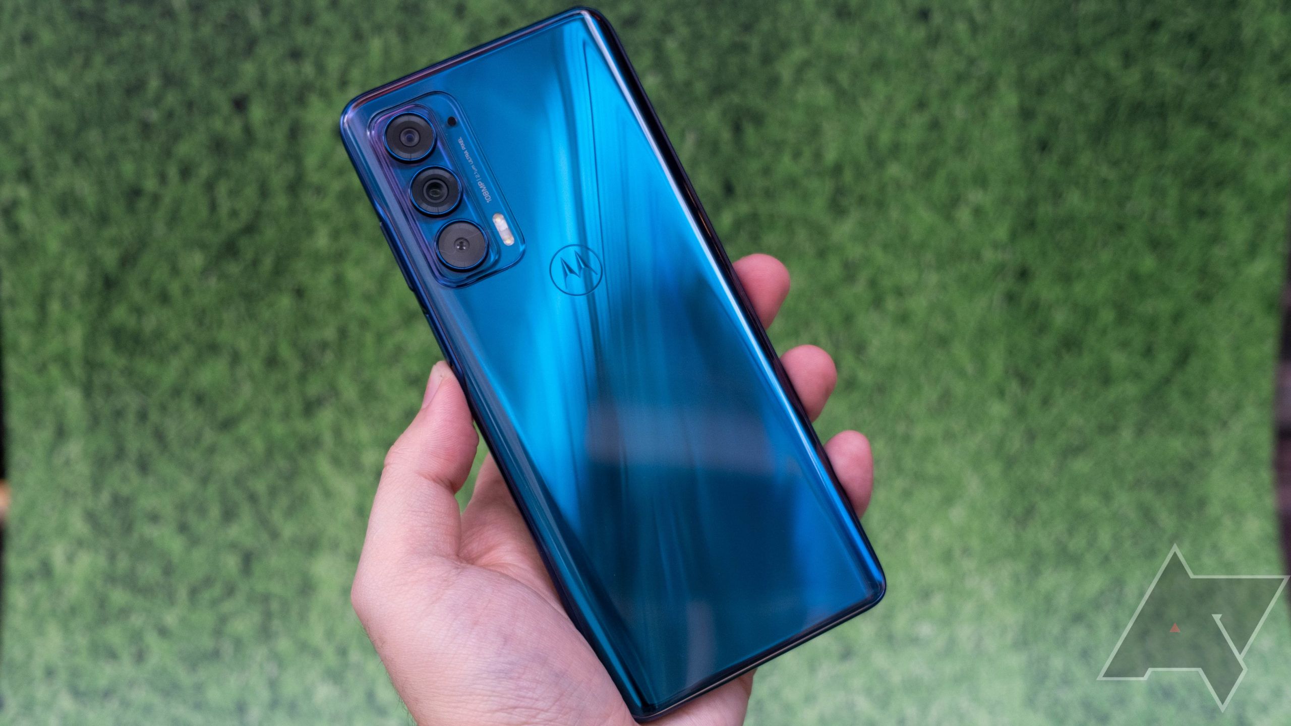 A hand holding the Moto Edge smartphone face down with the metallic blue case facing the camera. 