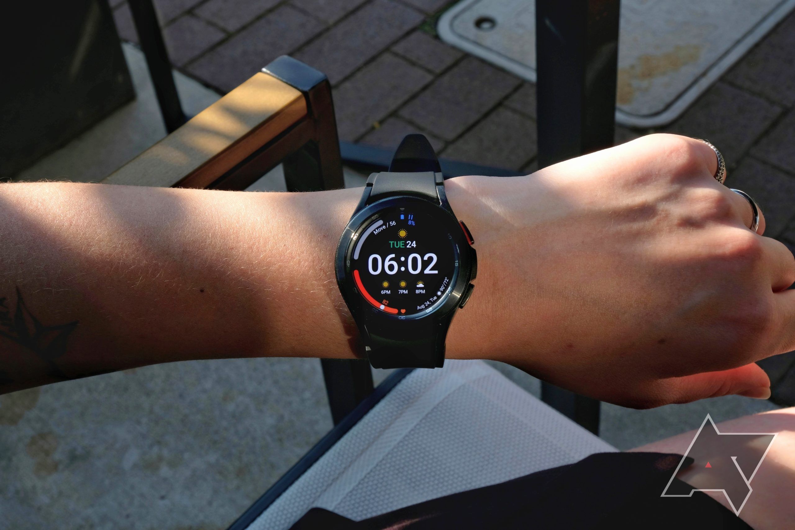 A person sitting outside wears a Samsung Galaxy Watch 4 on their left wrist.