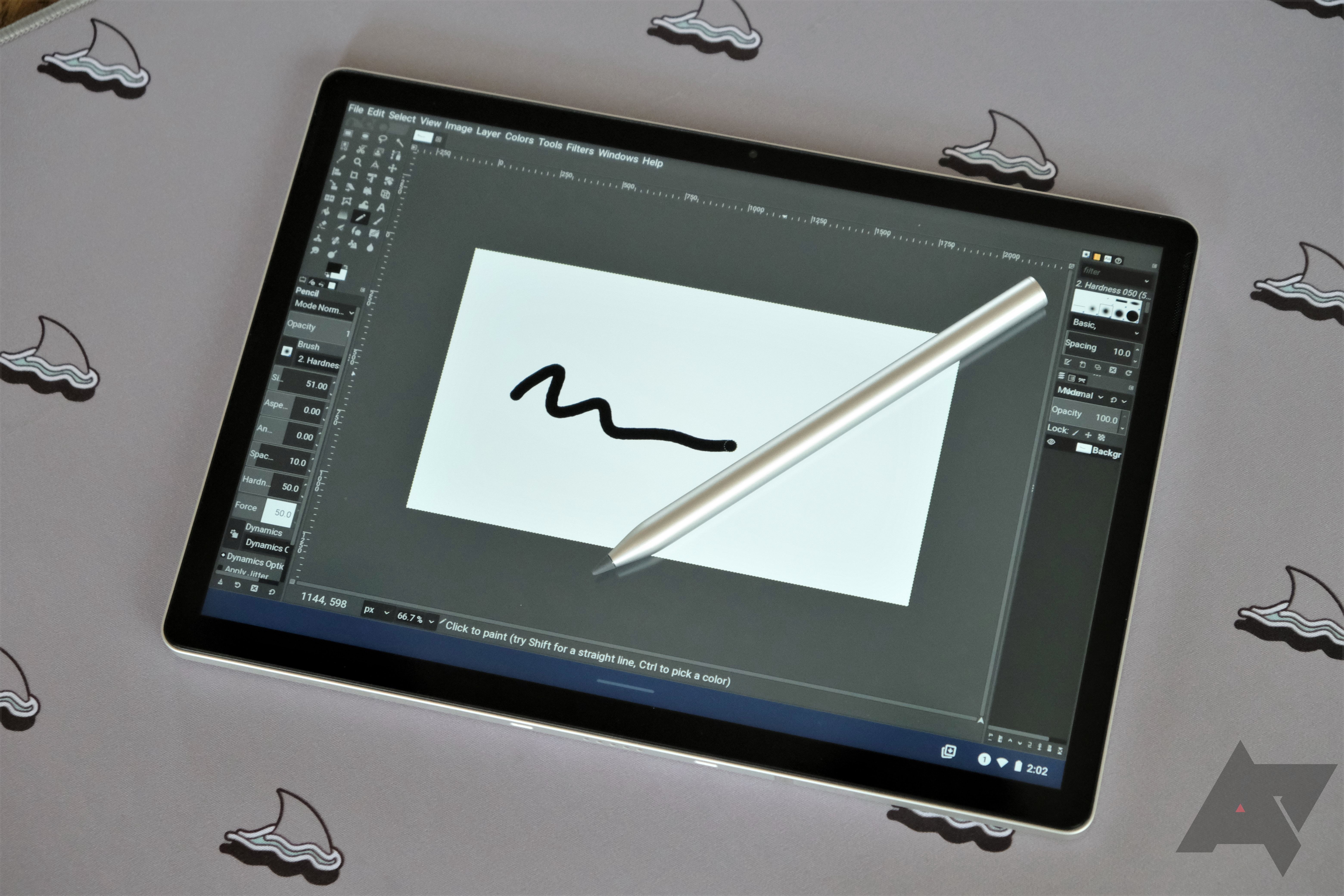 An HP Chromebook x2 11 in tablet mode with a pen on top of it and a drawing application open laying on a grey surface with shark fin images on it