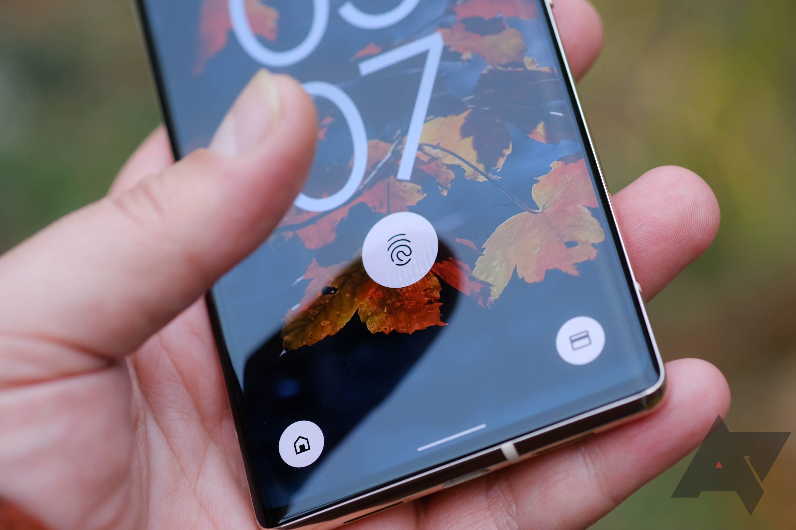 A person holding a Google Pixel phone on its lockscreen with their thumb hovering over the fingerprint sensor. 