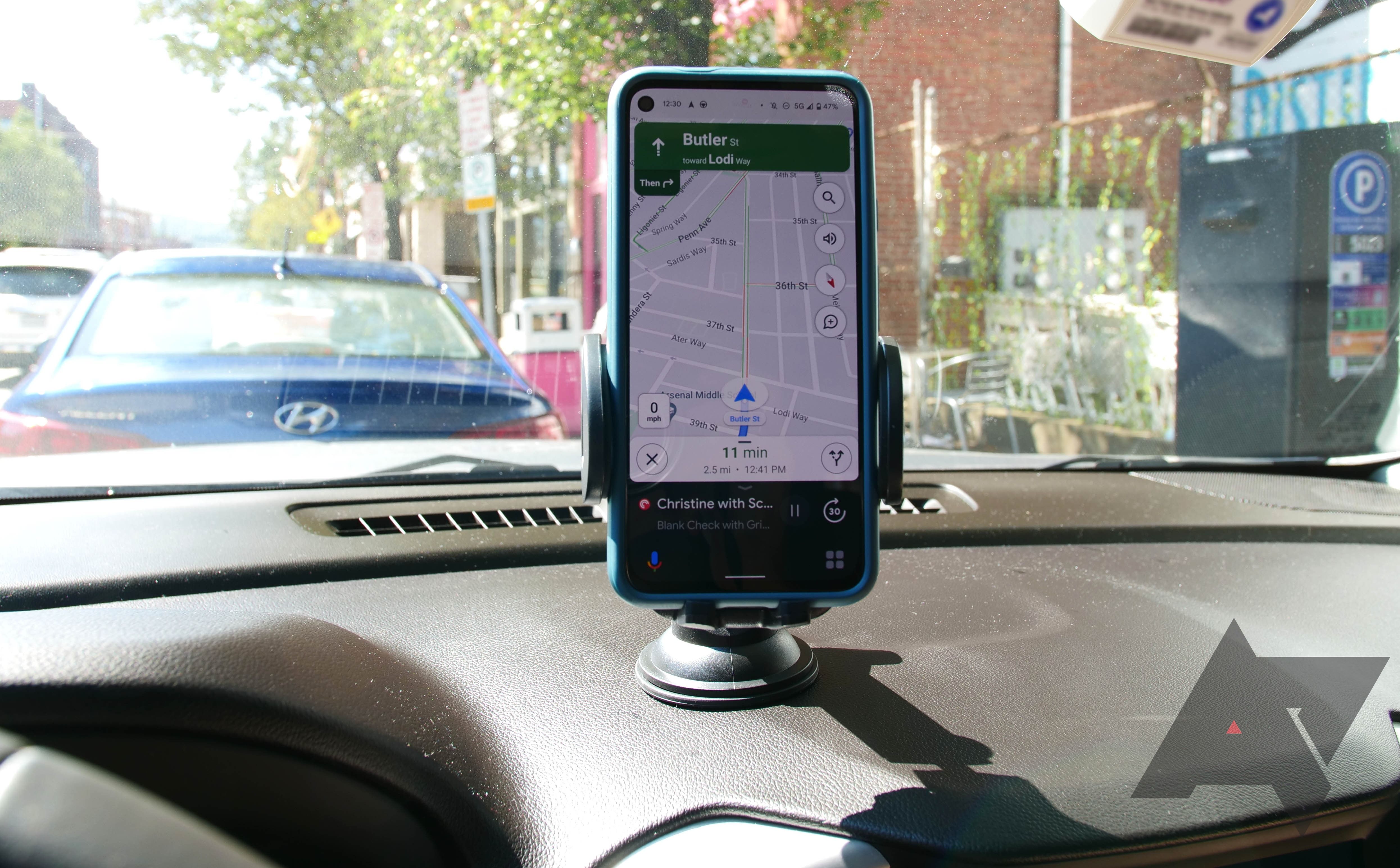 A phone running Assistant driving mode sitting in a dashboard mount with Maps displayed.