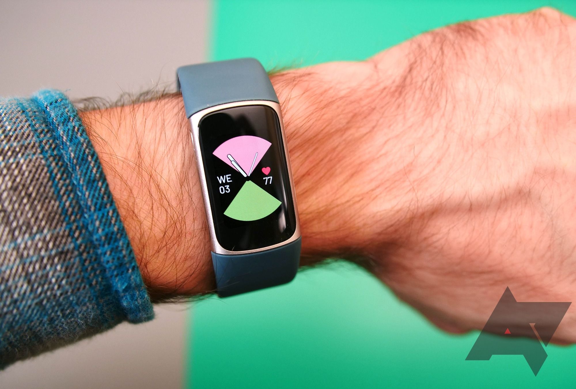 The watch face on a Fitibt charge 5 being worn on a wrist over a green background