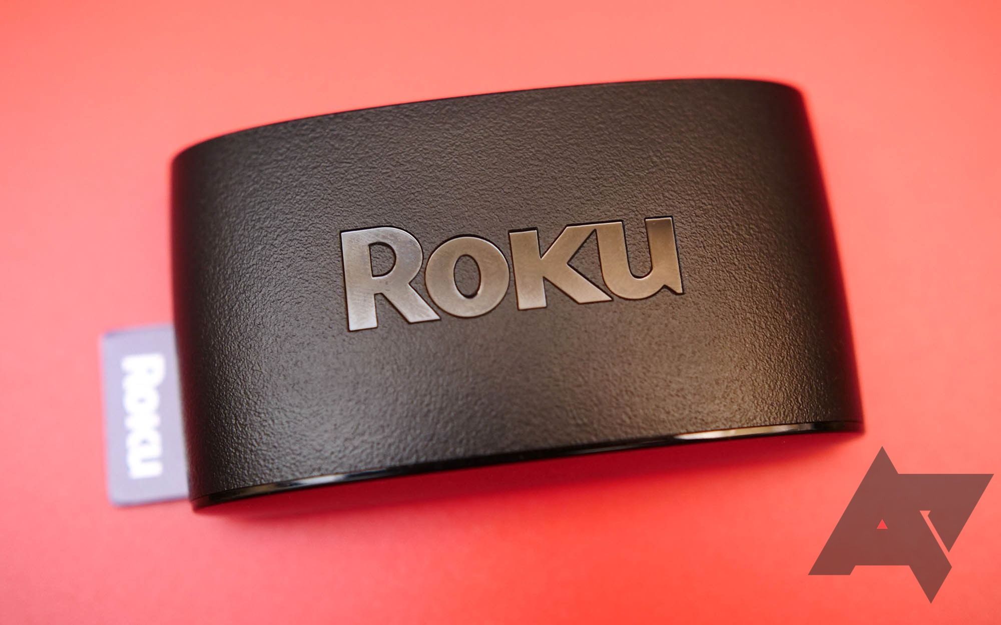Perangkat Roku hitam dengan latar belakang merah dengan logo Android Police di kanan bawah