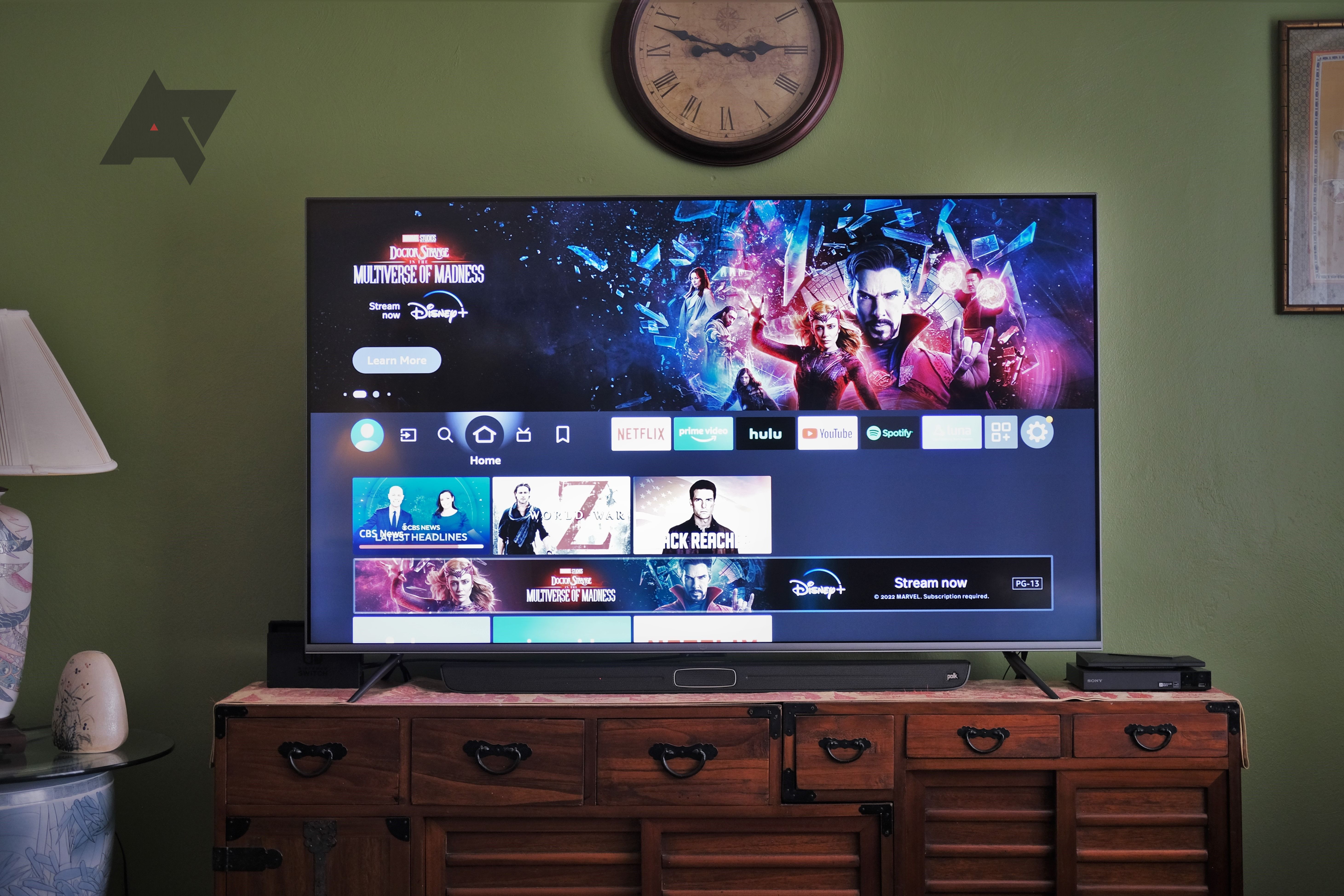 A powered-on smart TV sitting on a wooden entertainment center in front of a green wall.