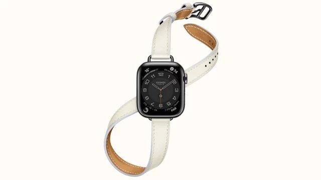 An Apple Watch with a black screen and white Hermé strap. 