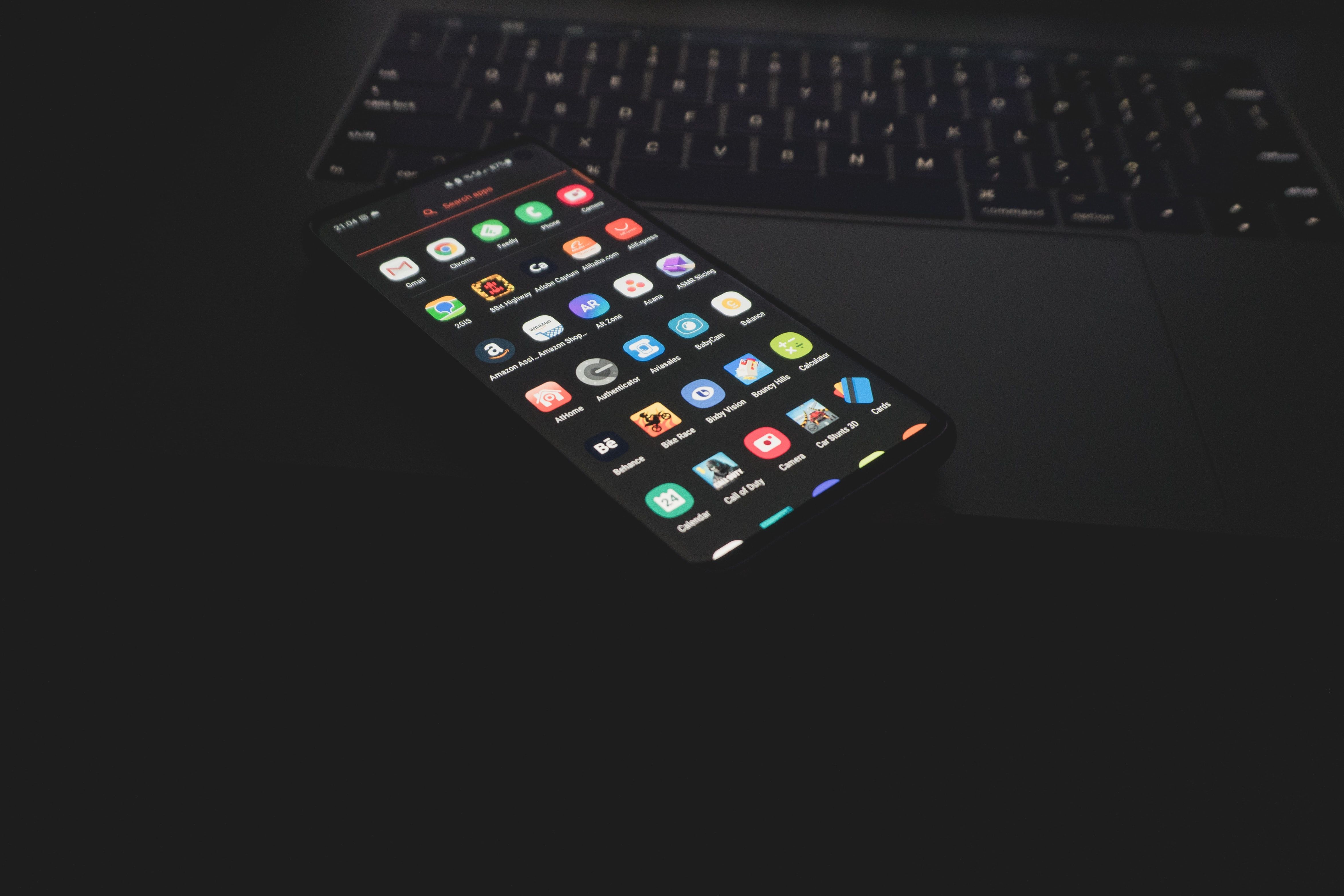 A imagem mostra um telefone Android aberto com ícones de aplicativos sobre o trackpad de um laptop.