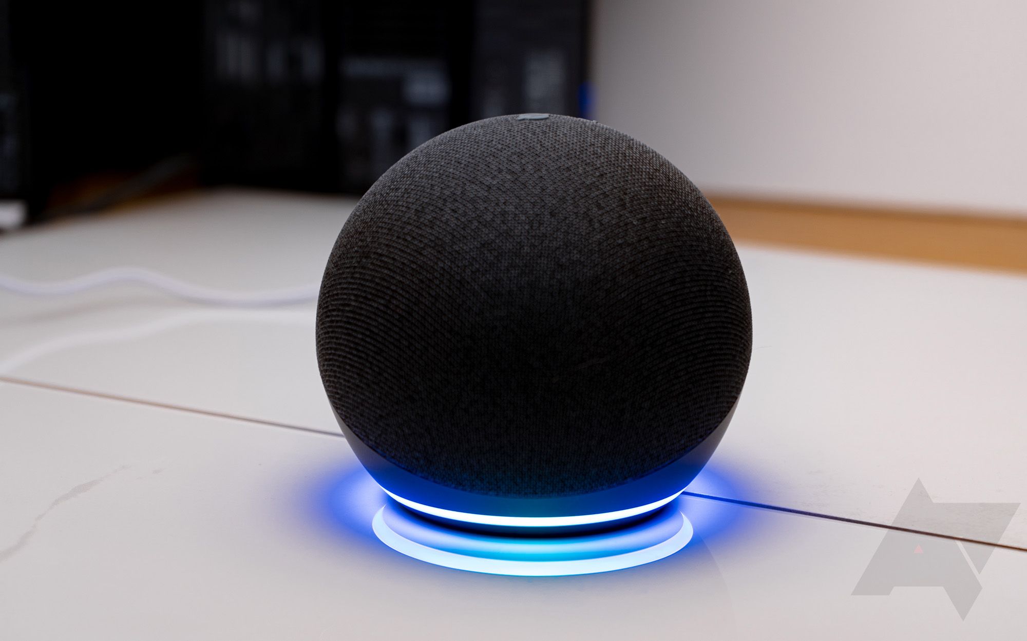 An Amazon Echo Dot 4th gen sitting on a table with the bottom ring lit up