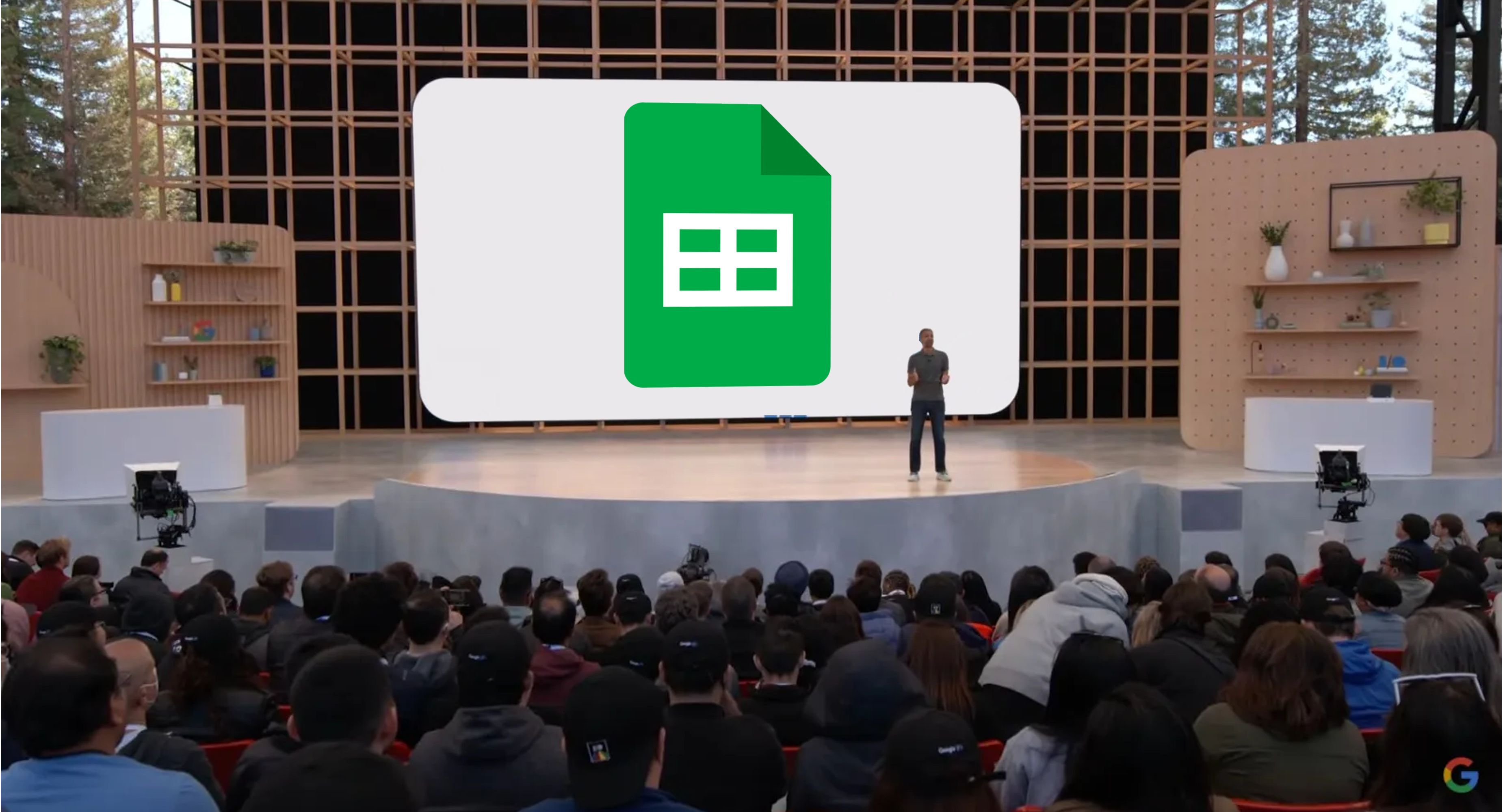 Seorang presenter google berdiri di depan layar presentasi dengan logo lembaran besar di atasnya