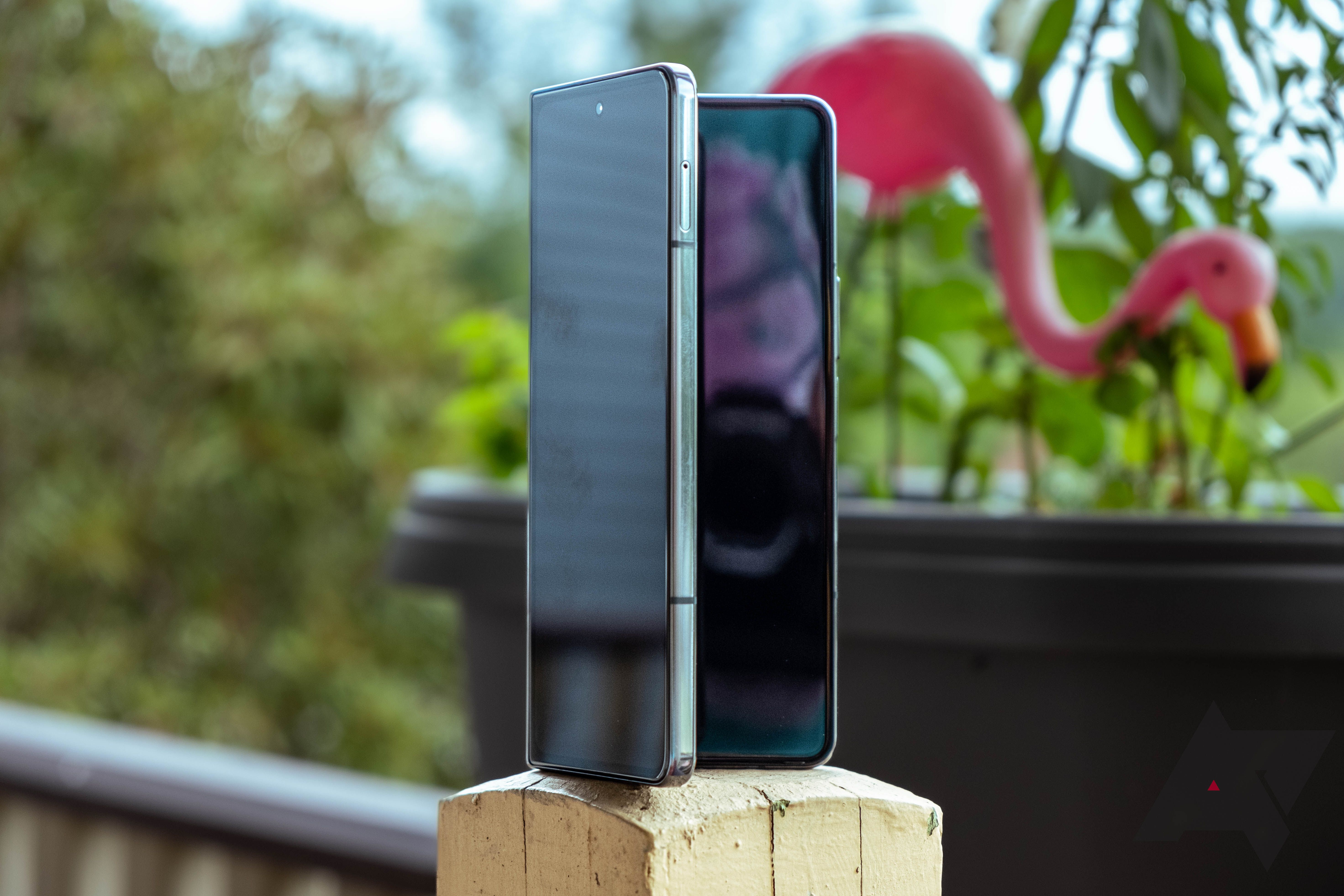 The Galaxy Z Fold 4 open and propped up on a fence post with a flamingo decoration in the background.