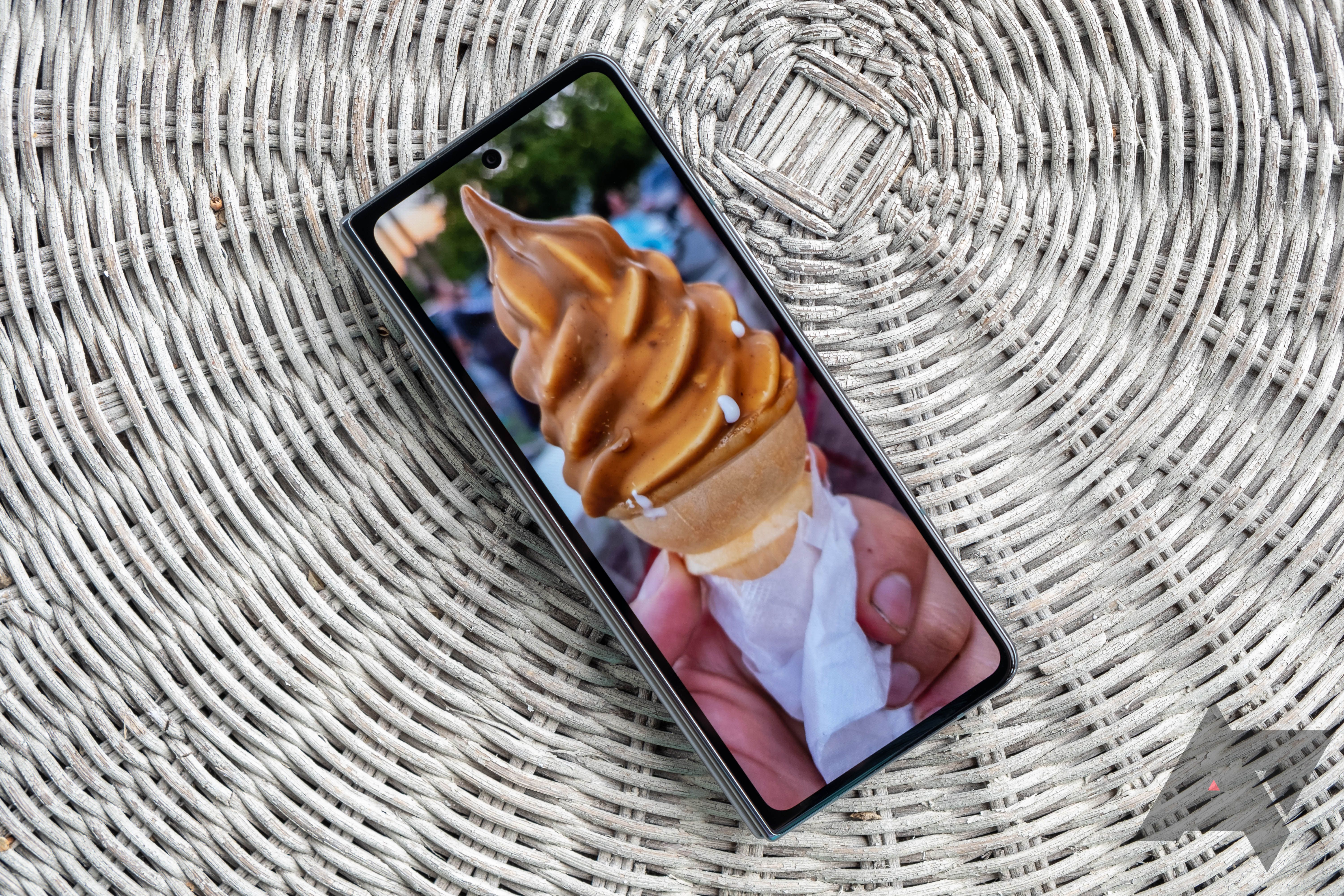 The Samsung Galaxy Fold 4 sitting on a wicker tabletop and showing an ice cream cone on its wallpaper