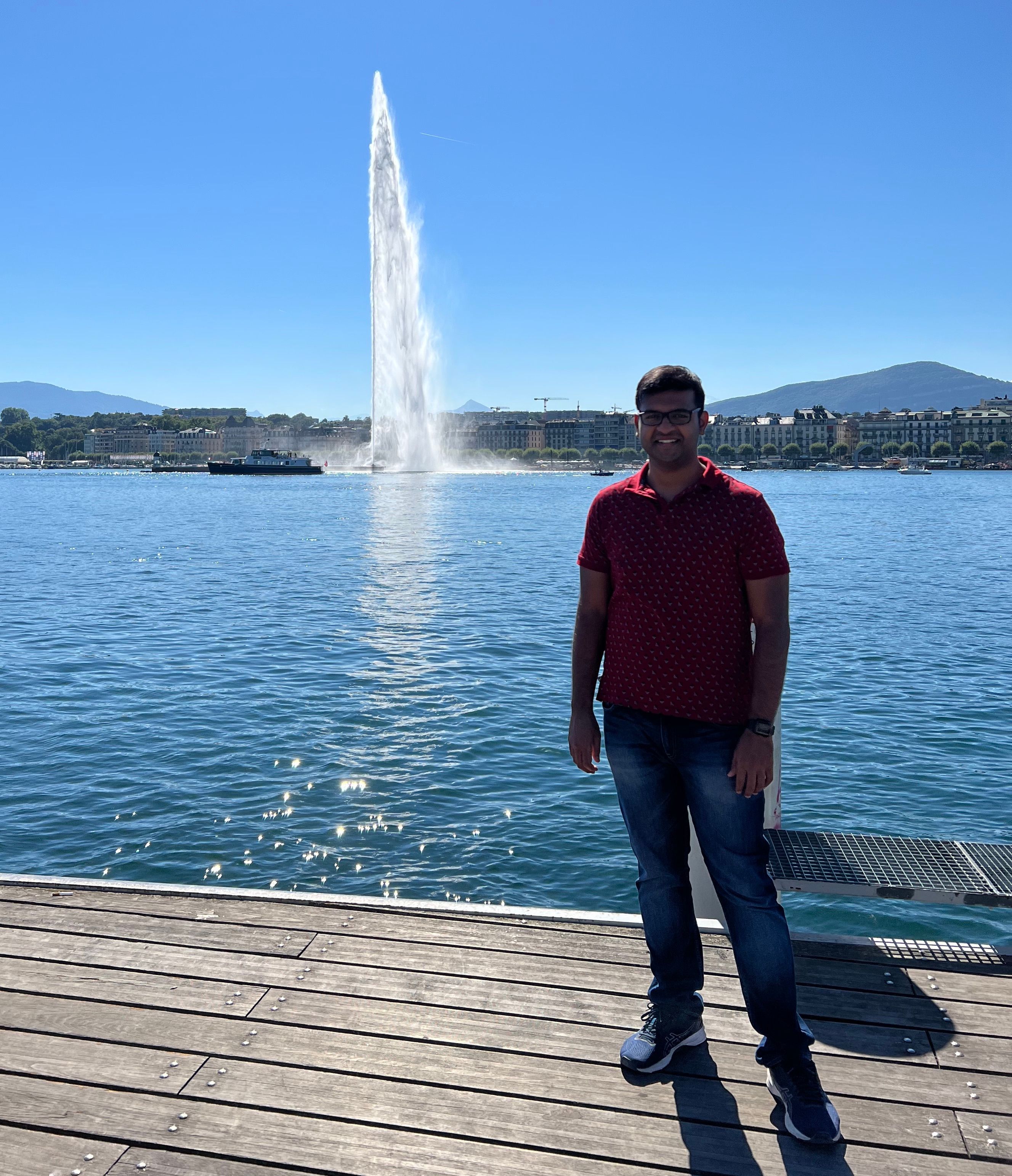 A person standing on a dock next to a lake with a fountain shooting into the air