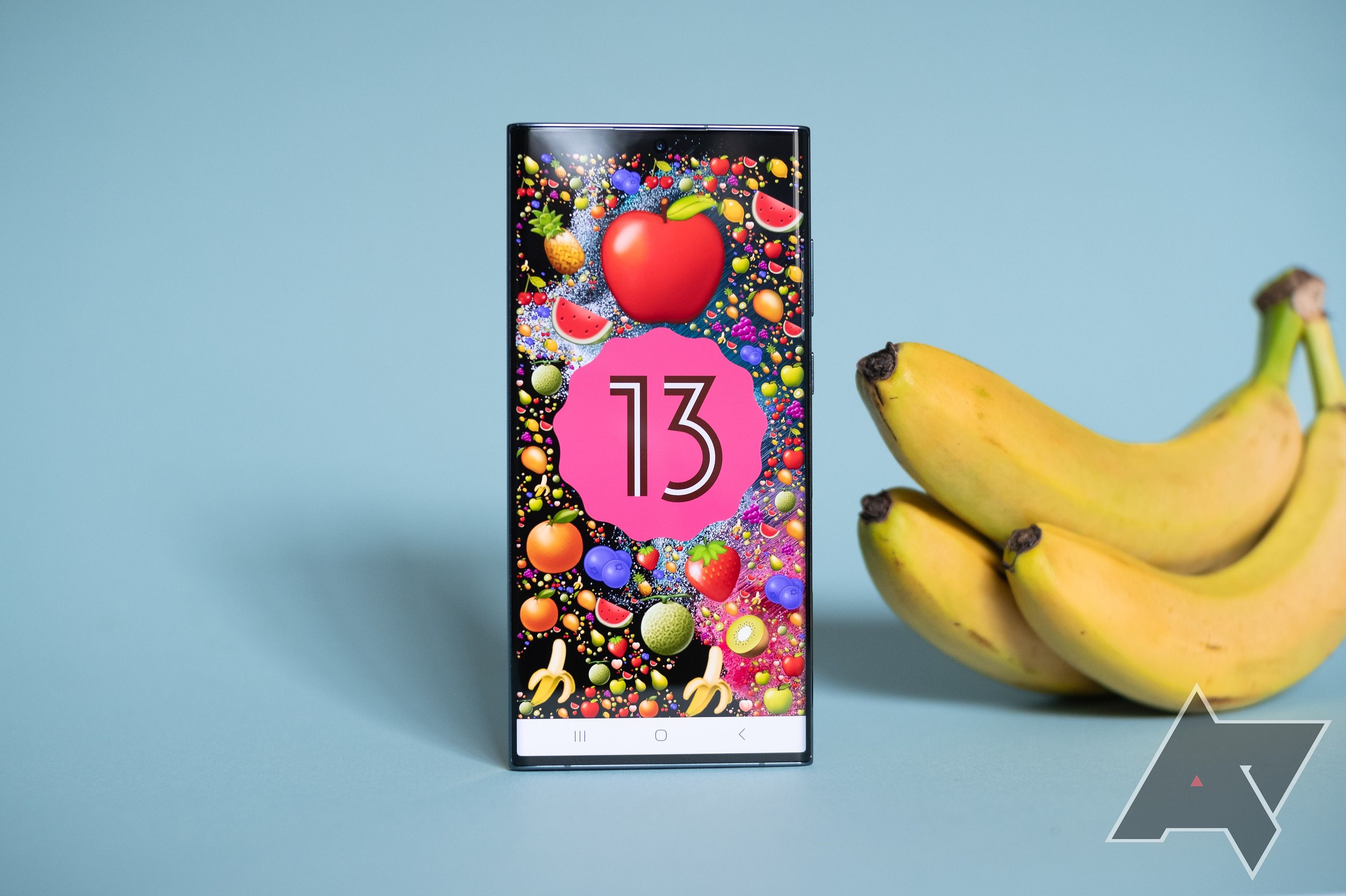 A Samsung Galaxy S22 Ultra, showing the Android 13 emoji easter egg, sitting next to a bunch of bananas.