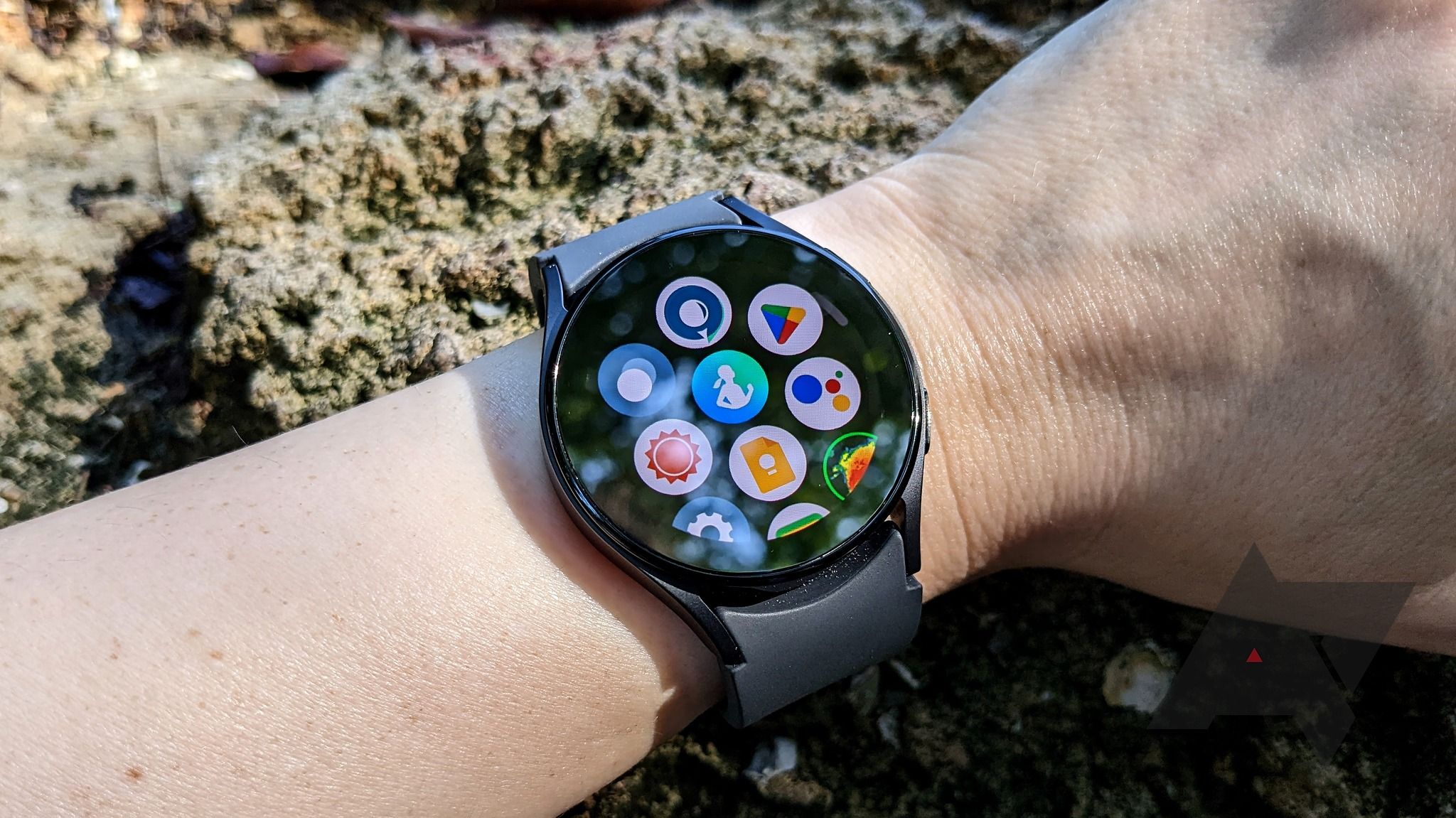 Galaxy Watch 5 being worn on a wrist in front of a rocky background with the app drawer screen on