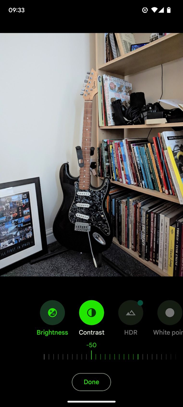 black electric guitar standing next to bookshelf and picture frame