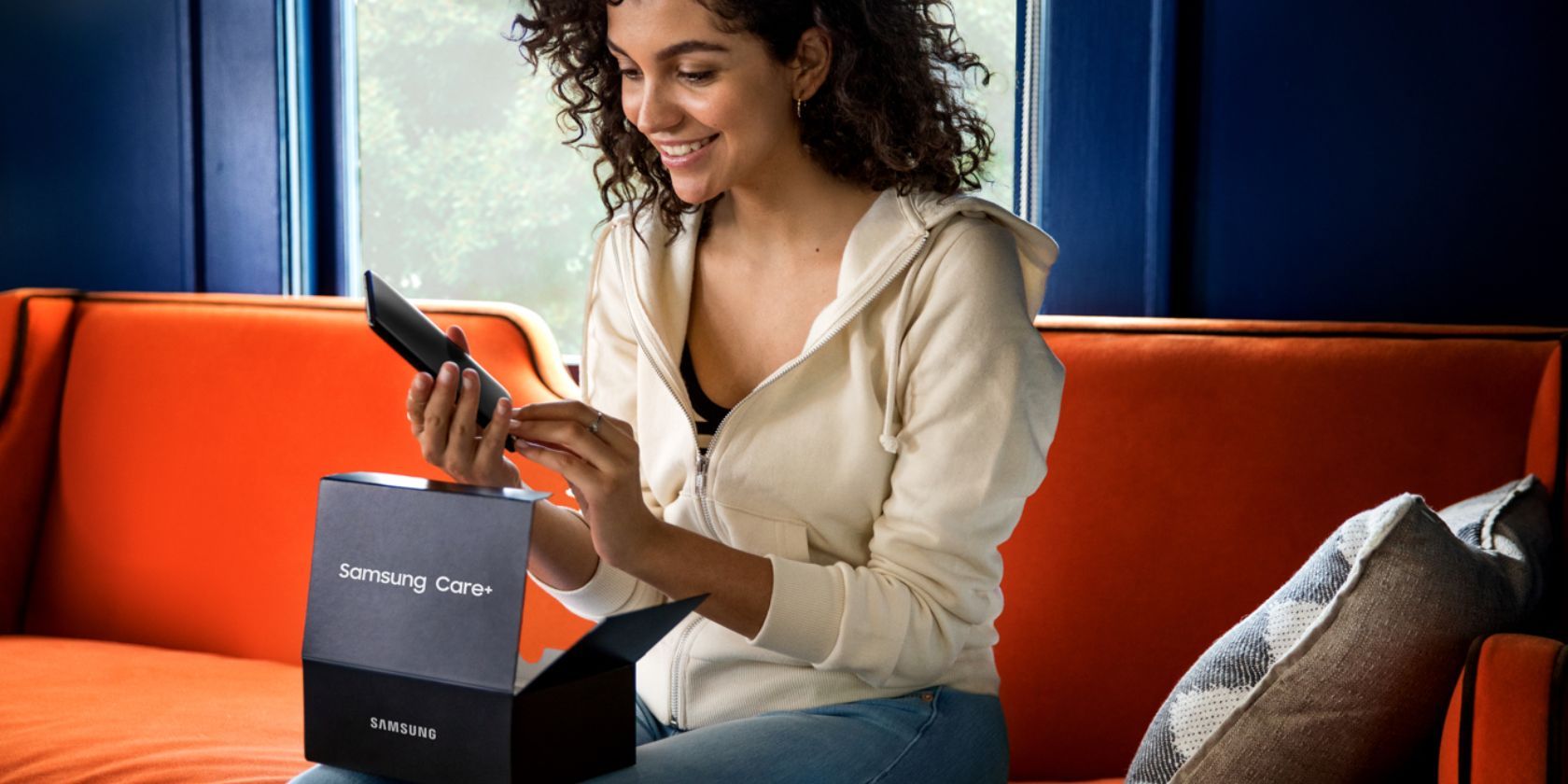 A person opening a Samsung Care+ package and holding a phone