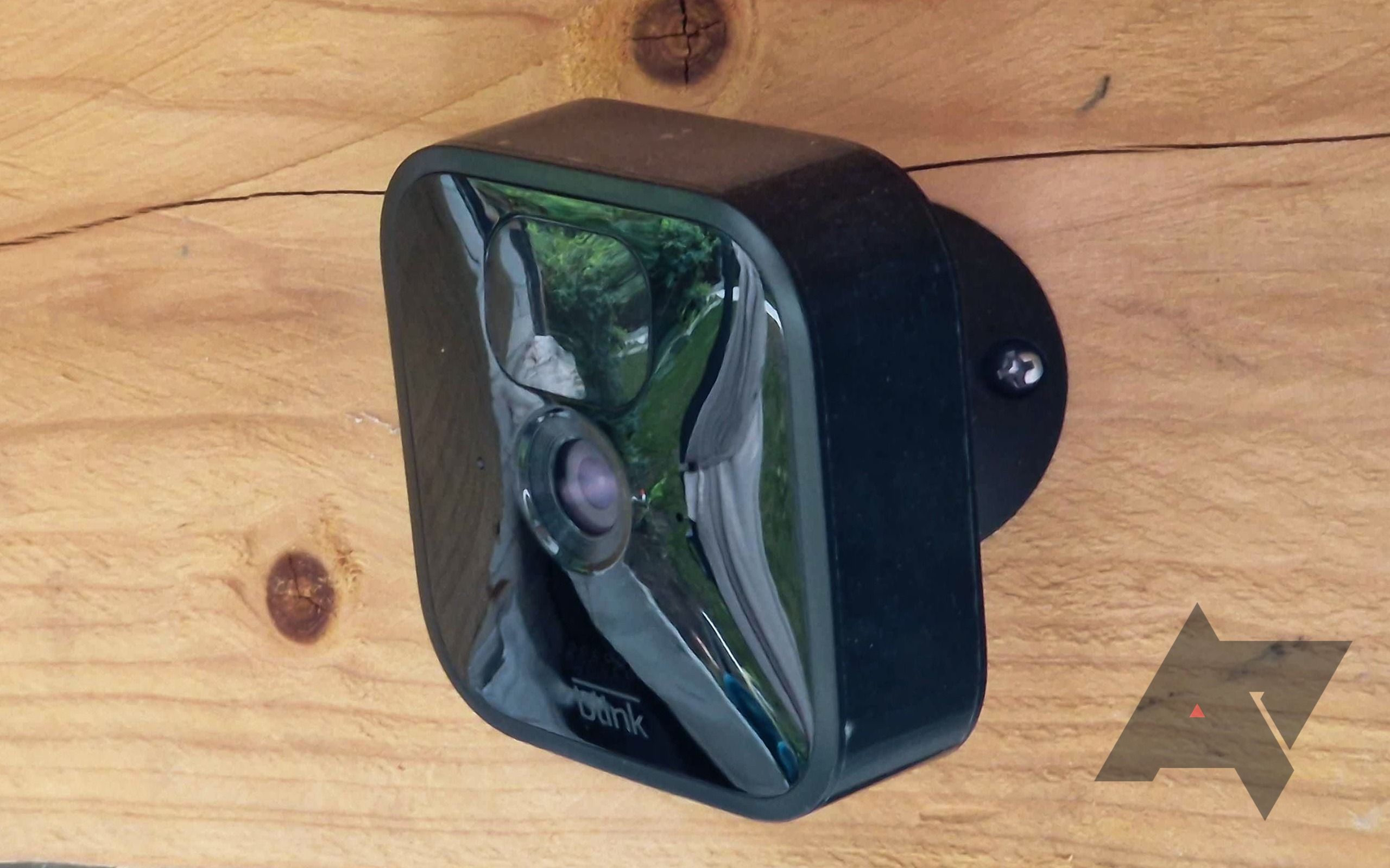 A Blink outdoor camera mounted on a piece of wood.