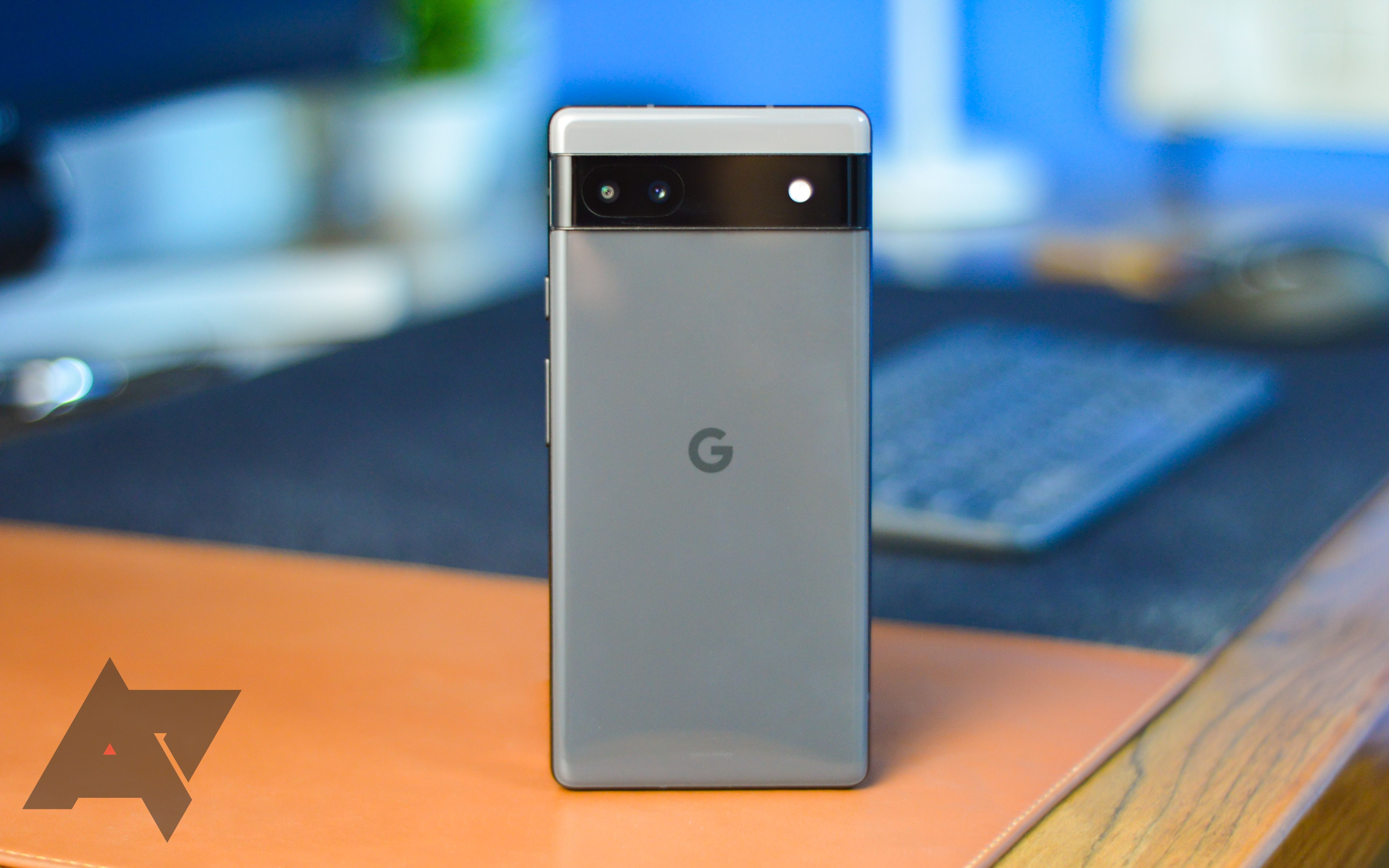 Google Pixel 6a abu-abu berdiri di atas meja tulis kulit warna unta.