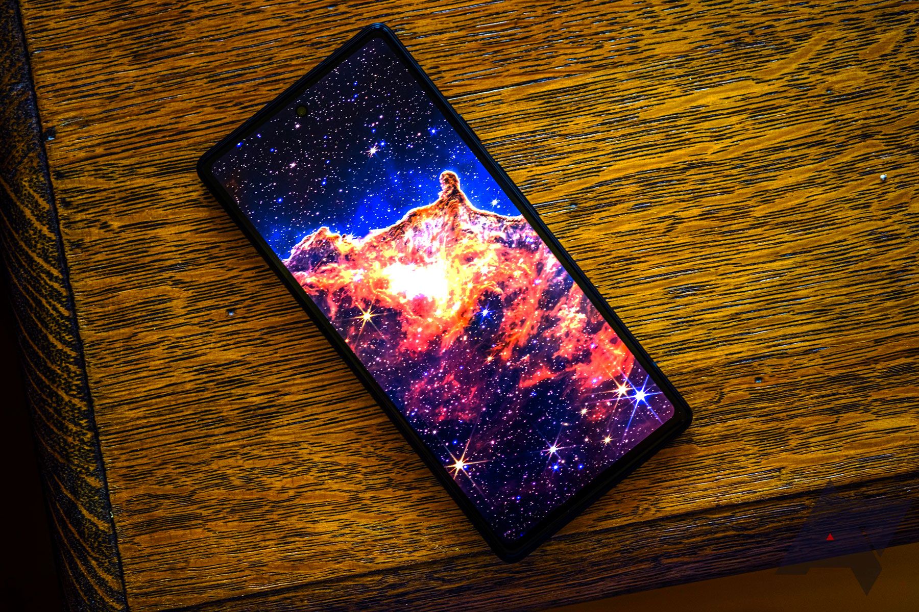 A phone with an illuminated display sits atop a woodgrain table. 