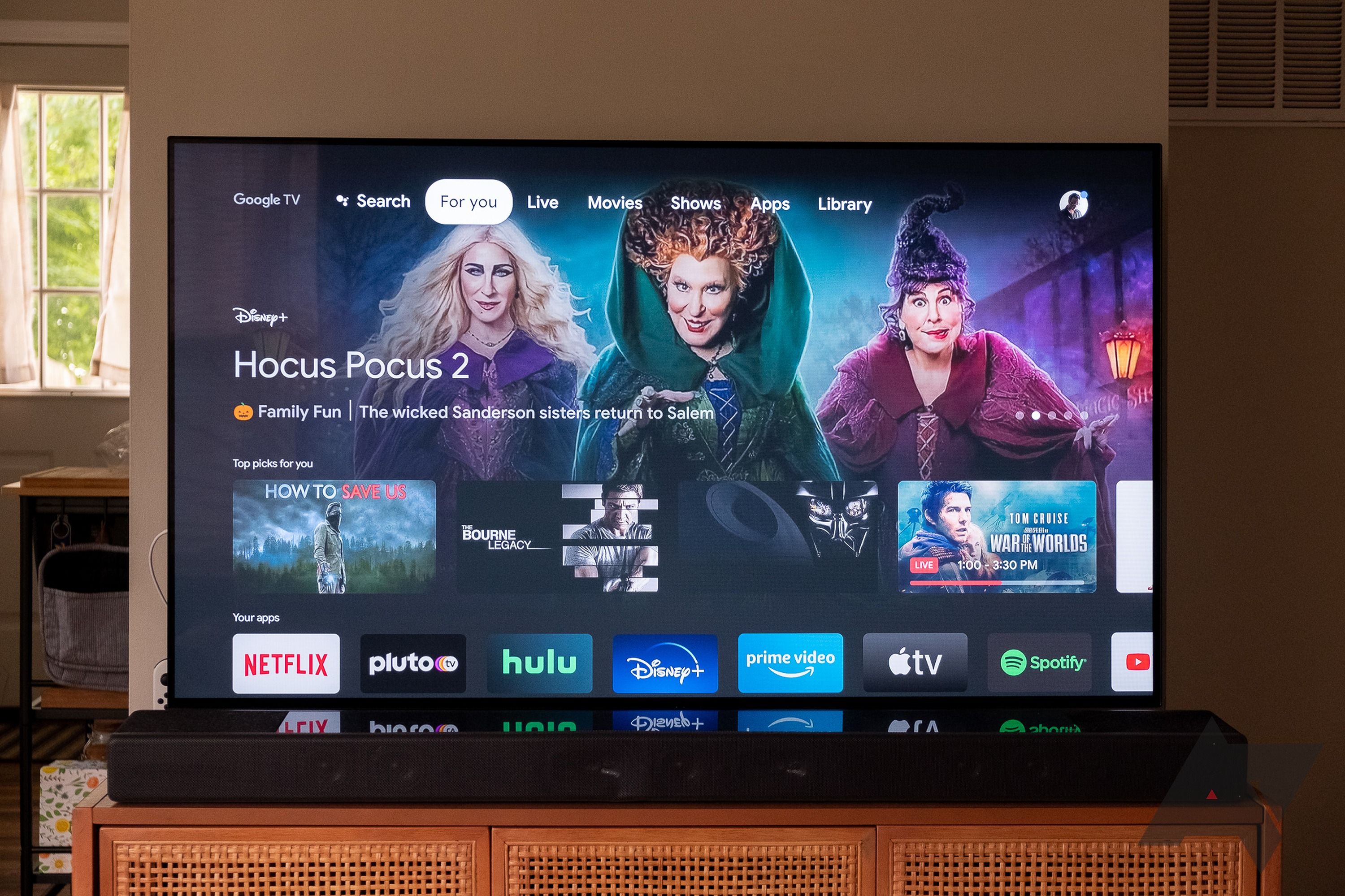 TV besar dengan dudukan di rumah dengan layar utama Google TV ditampilkan.