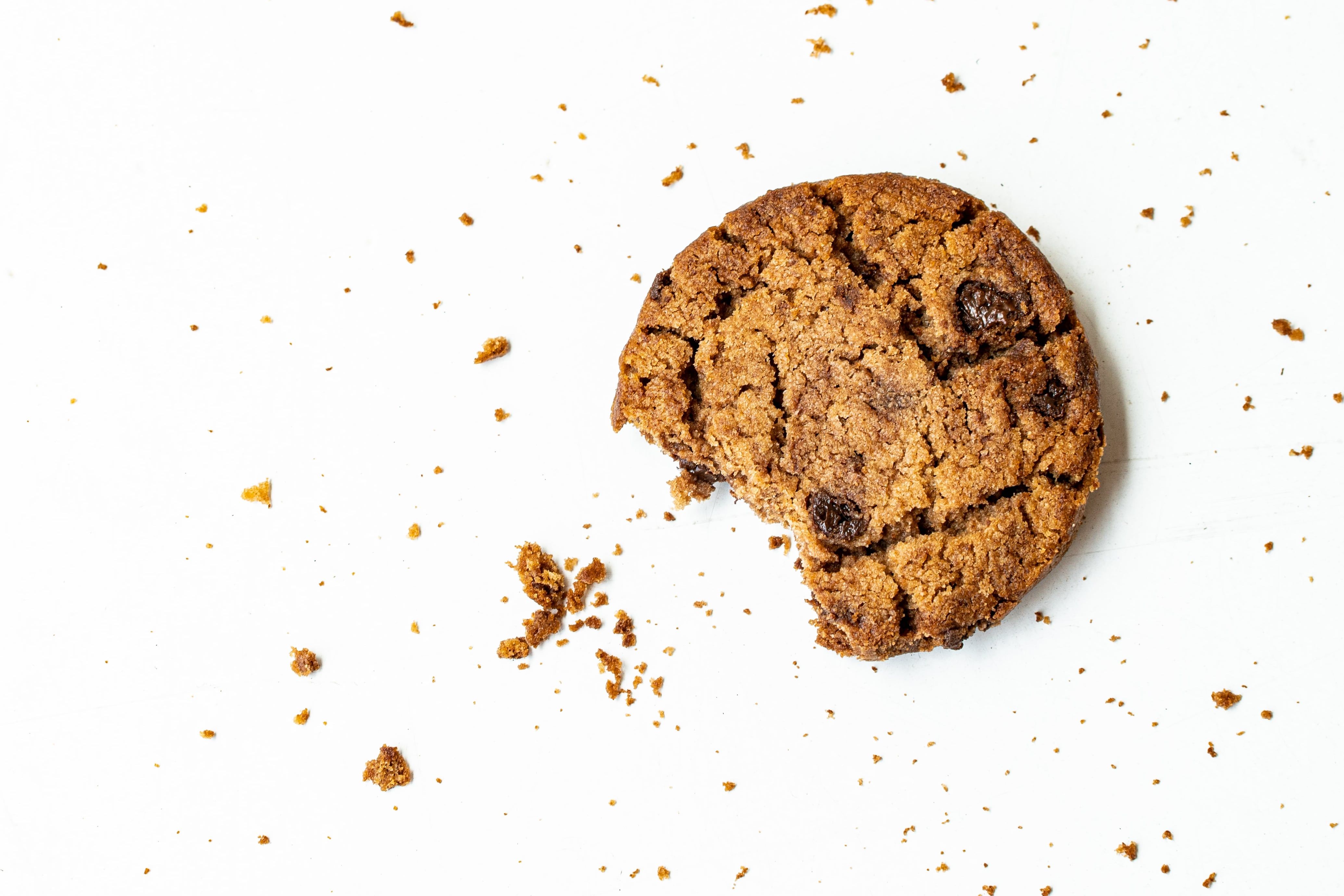 A cookie with a bite taken out and crumbs against a white background.