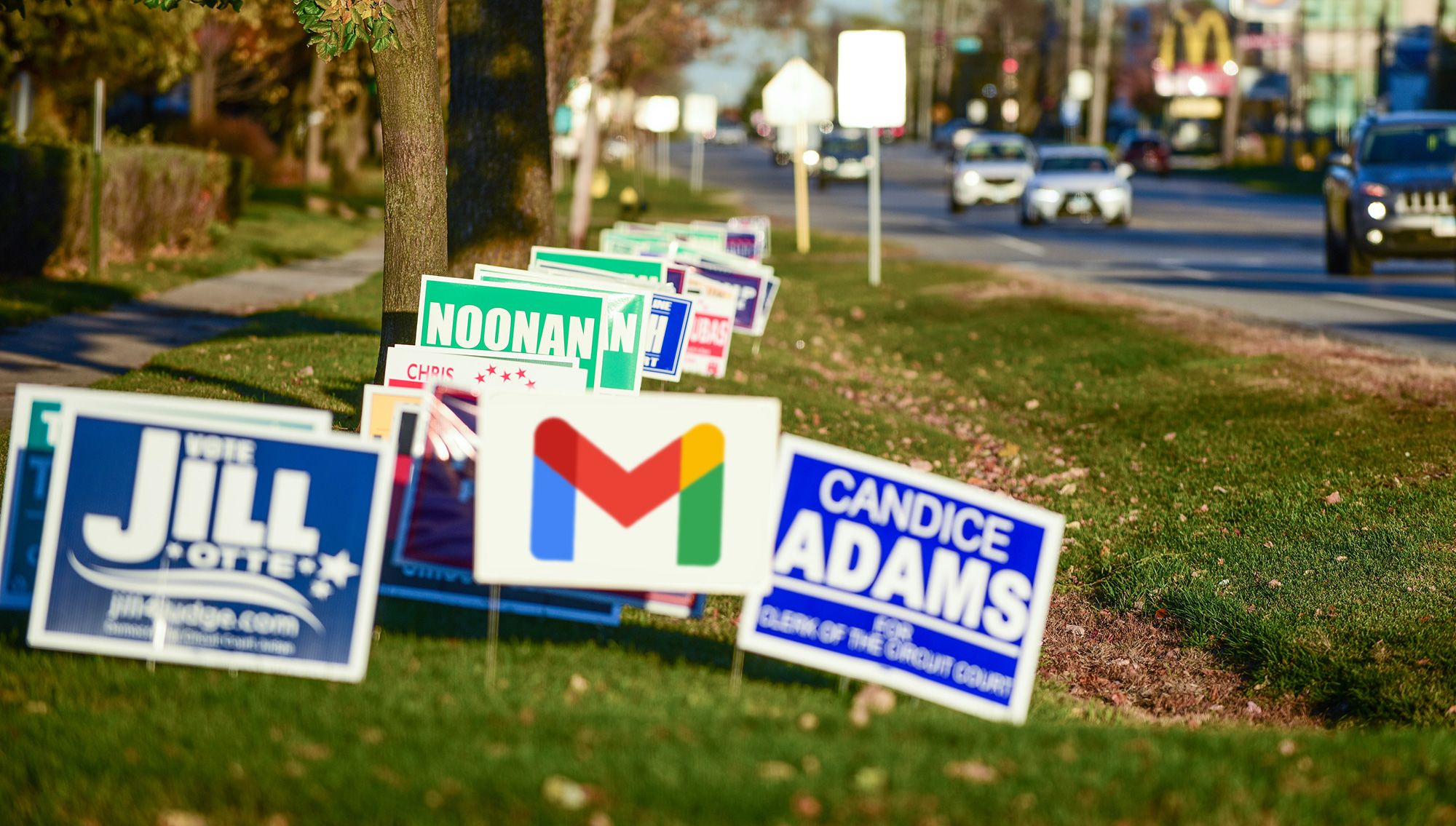 A grassy area next to a road is filled with political campaign signs, with the Google Gmail logo in the middle
