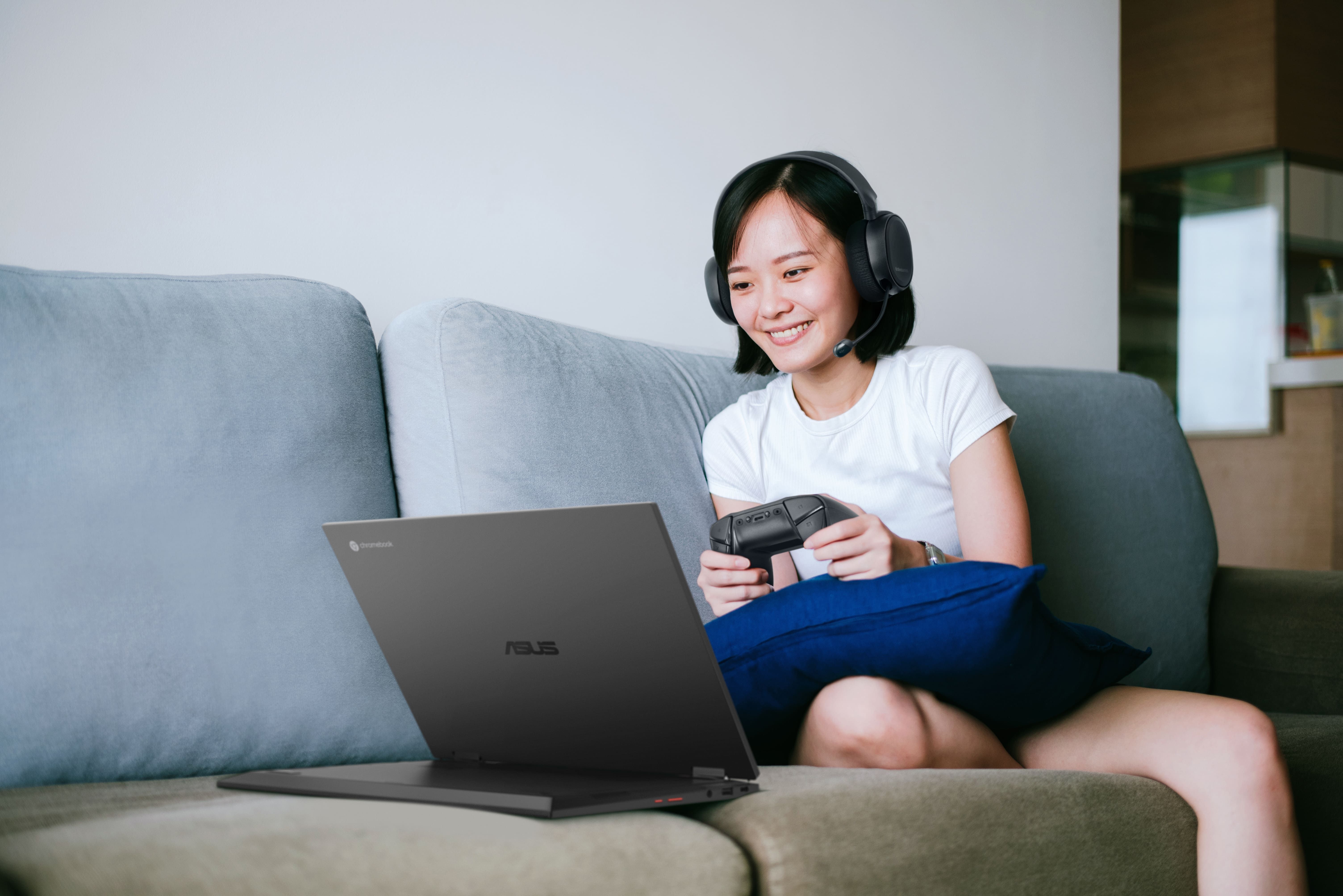 A woman wears headphones and a controller in front a of laptop that's tilted back in display mode.
