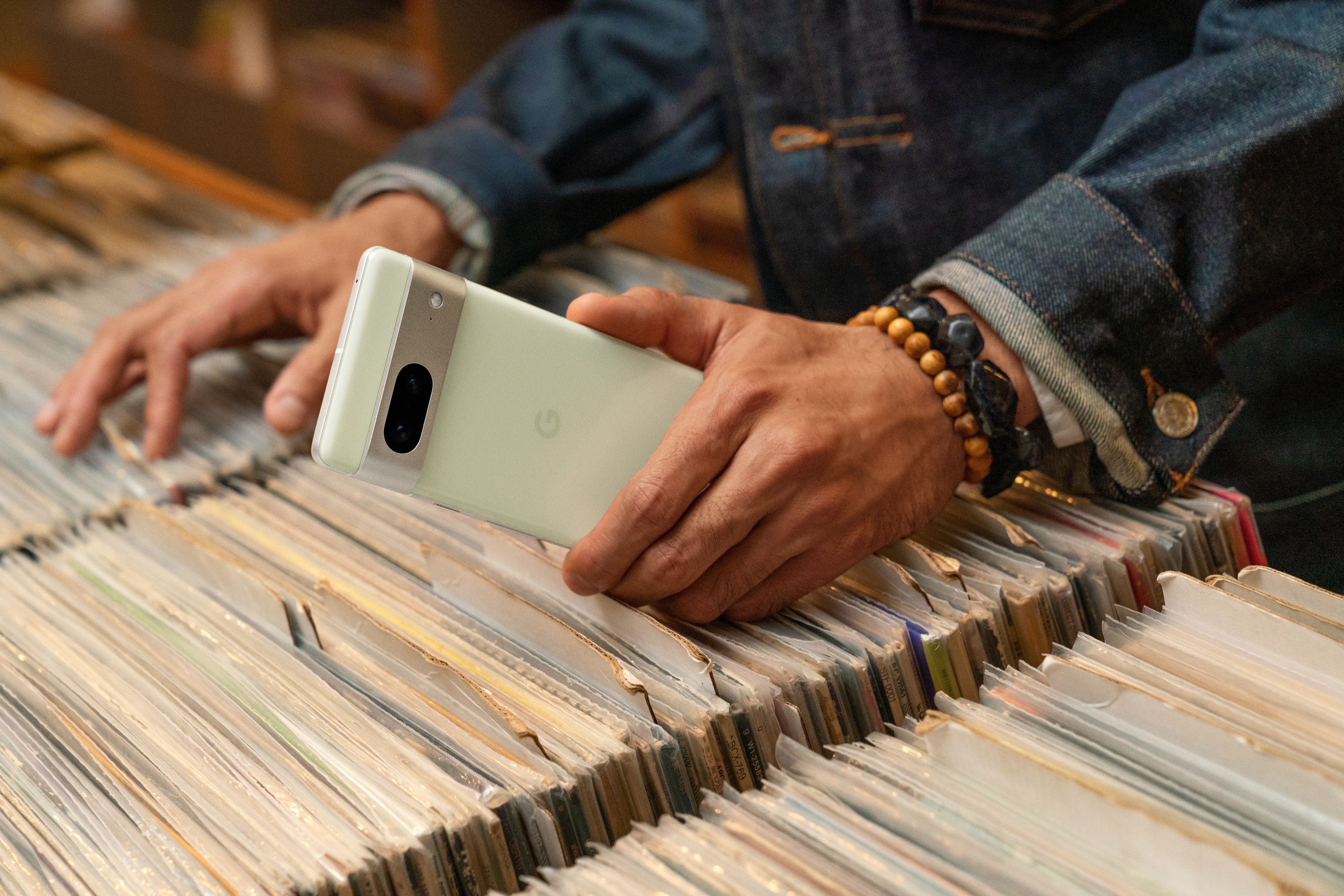 A person browsing through a stack of records and holding a Google Pixel phone