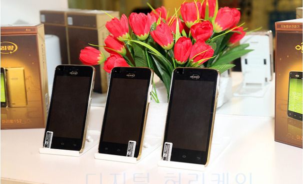 three smartphones with screens off on stands in front of flowers