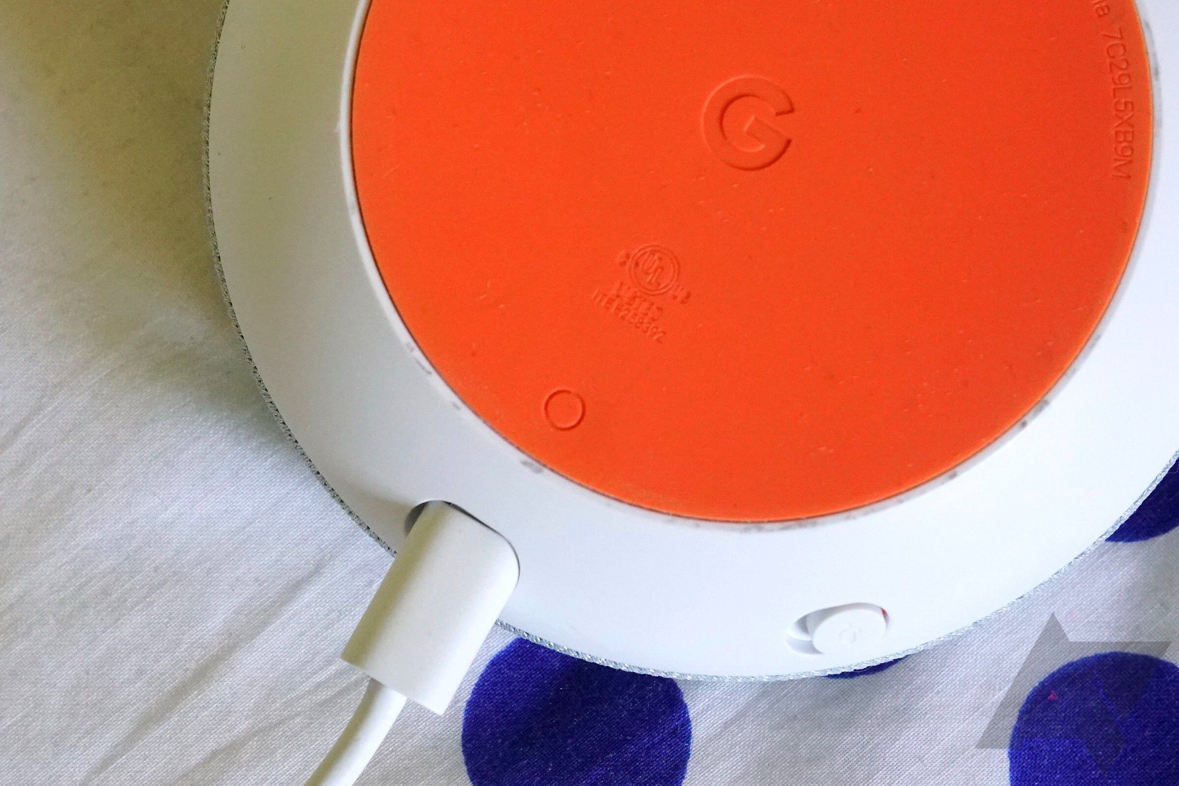 The bottom of a Google Home Mini speaker showing its power cord and reset button