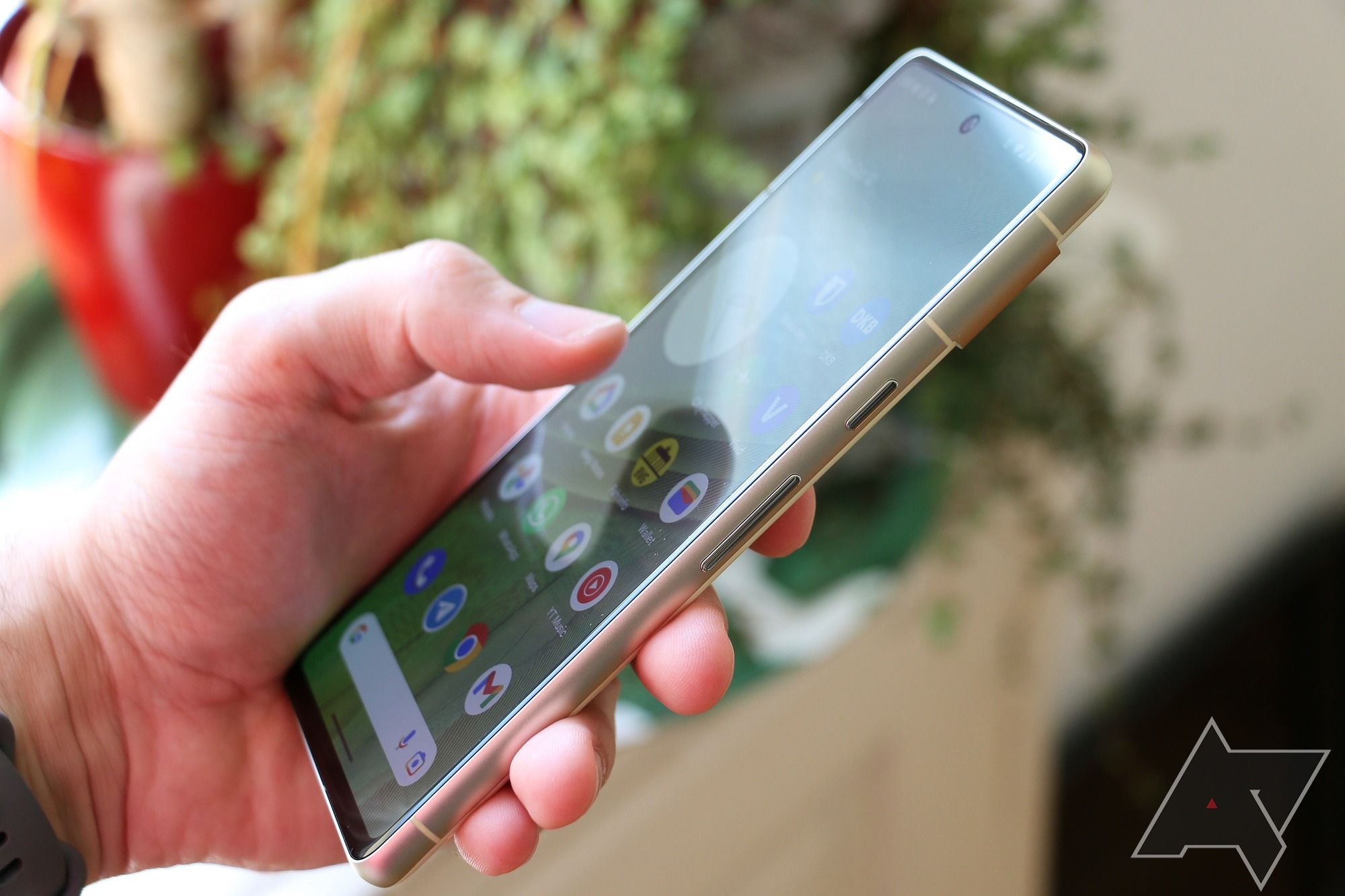 The Google Pixel 7 with display turned on, held in a left hand with a plant in the background