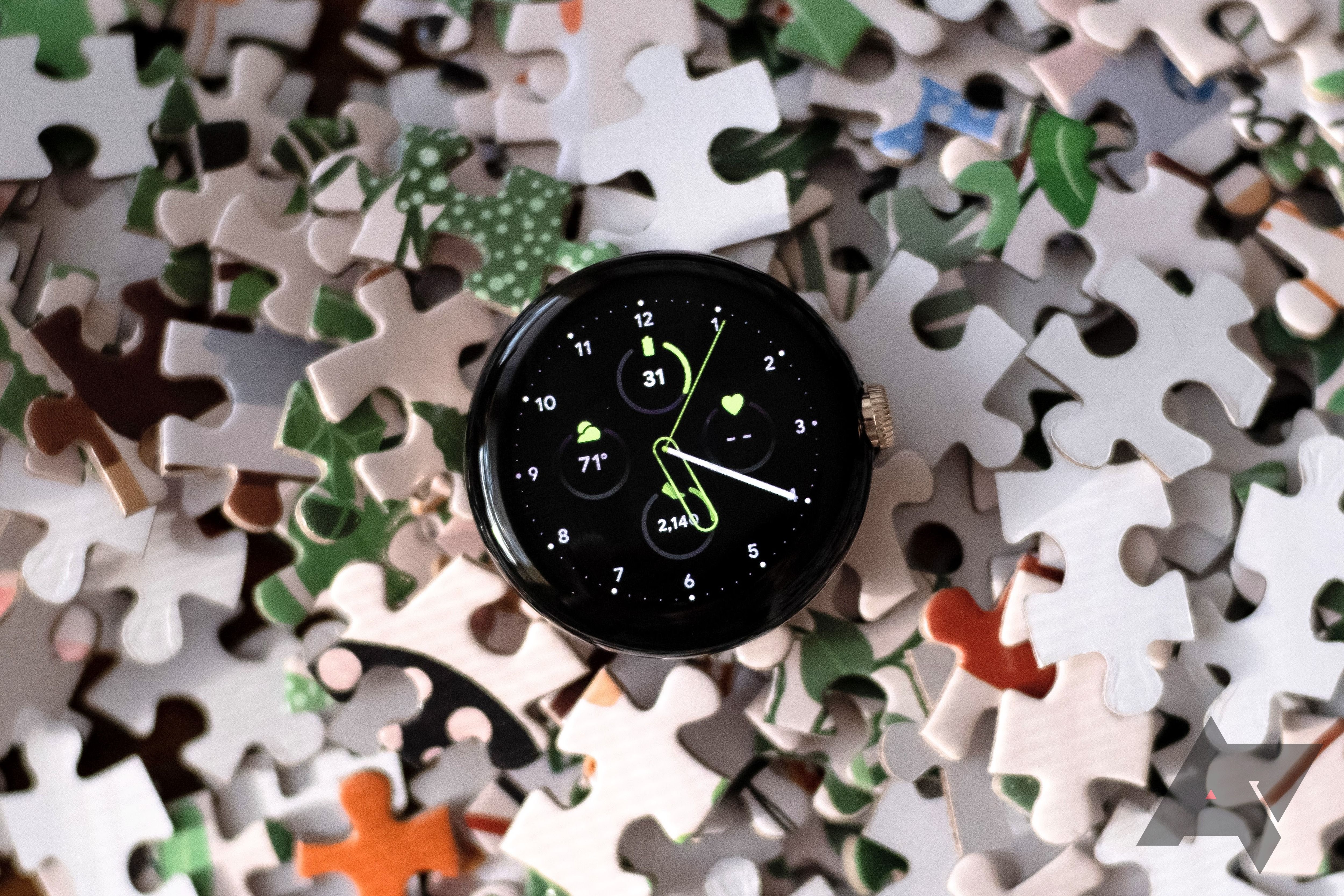 A round smartwatch body on a pile of jigsaw puzzle pieces.