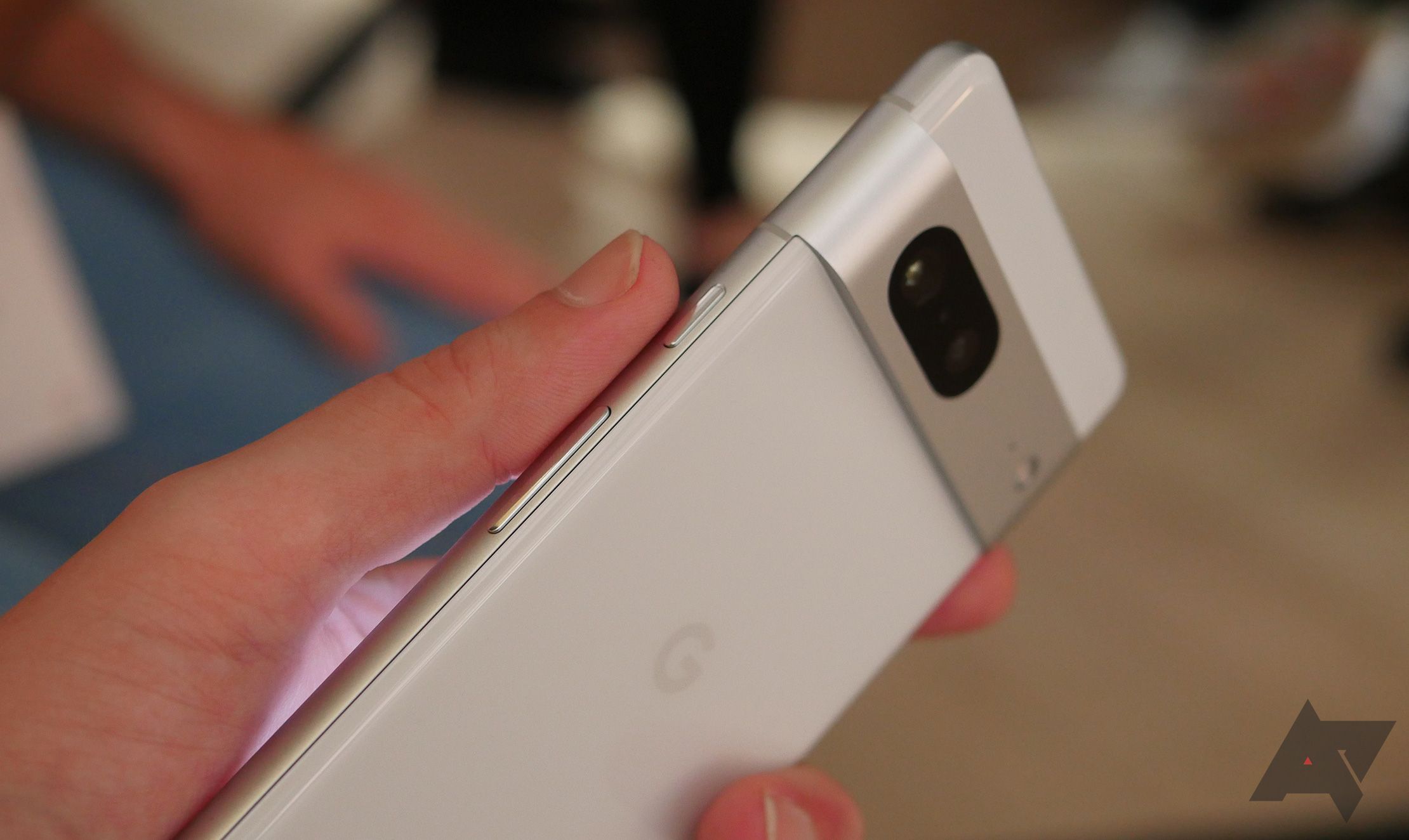 Sebuah tangan memegang Google Pixel 7 dan menunjukkan tombol samping telepon