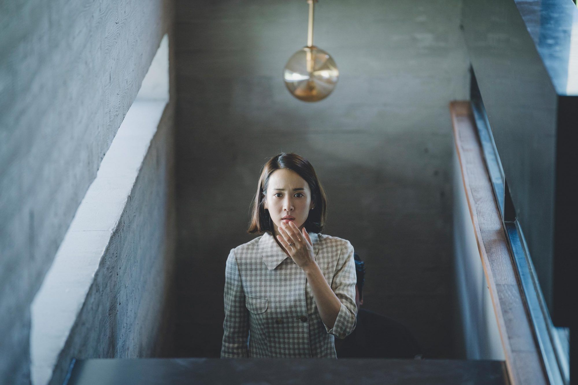 A woman stands in a stairwell with her left hand in front of her mouth. 