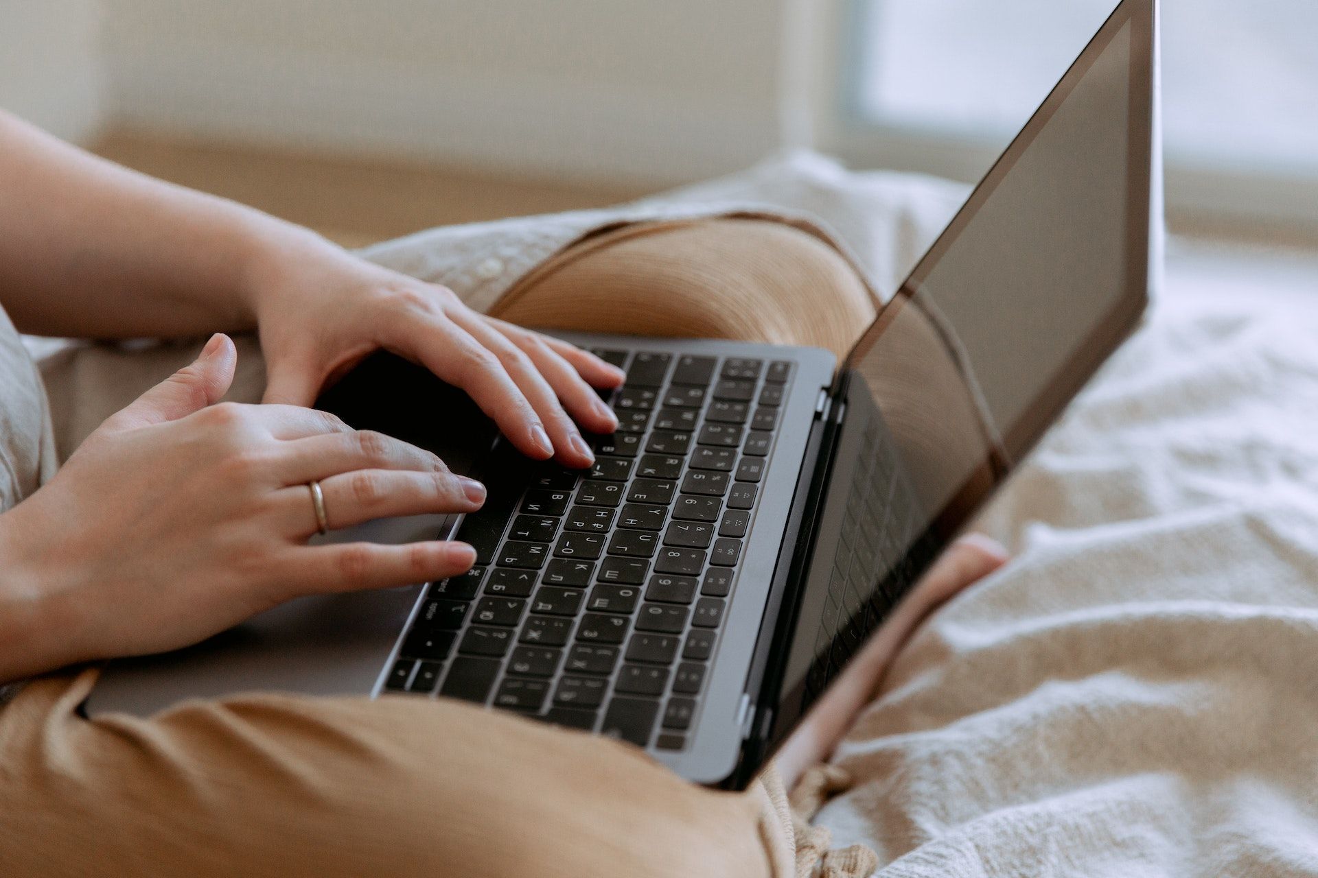 A cropped image of a person wearing camel pants with a laptop in their lap.