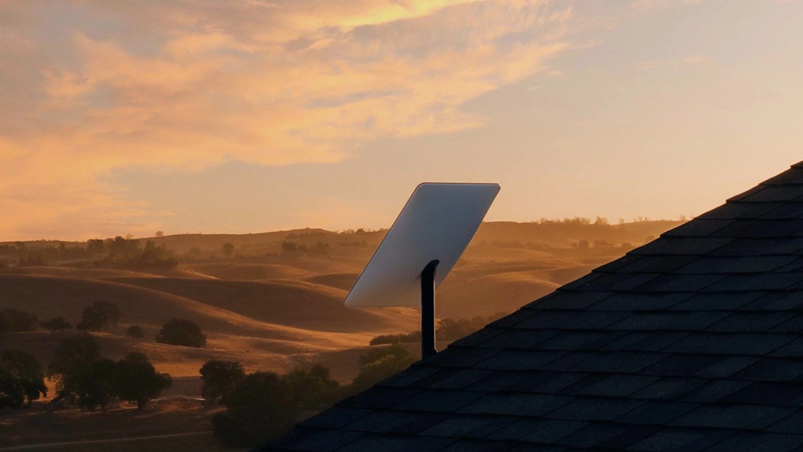 A starlink receiver aspects in direction of the hills below a sundown.