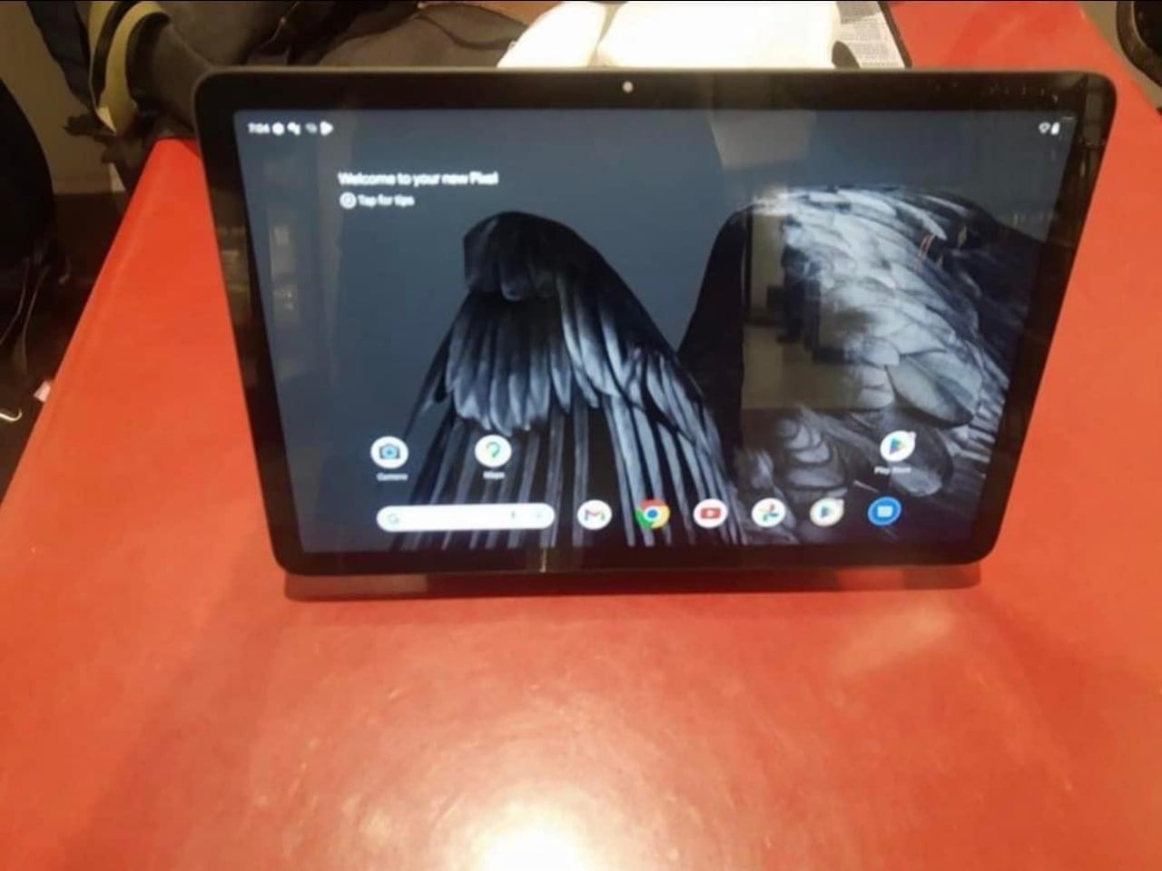 A tablet, reportedly the Google Pixel Tablet, sits atop a red table with its display illuminated. 