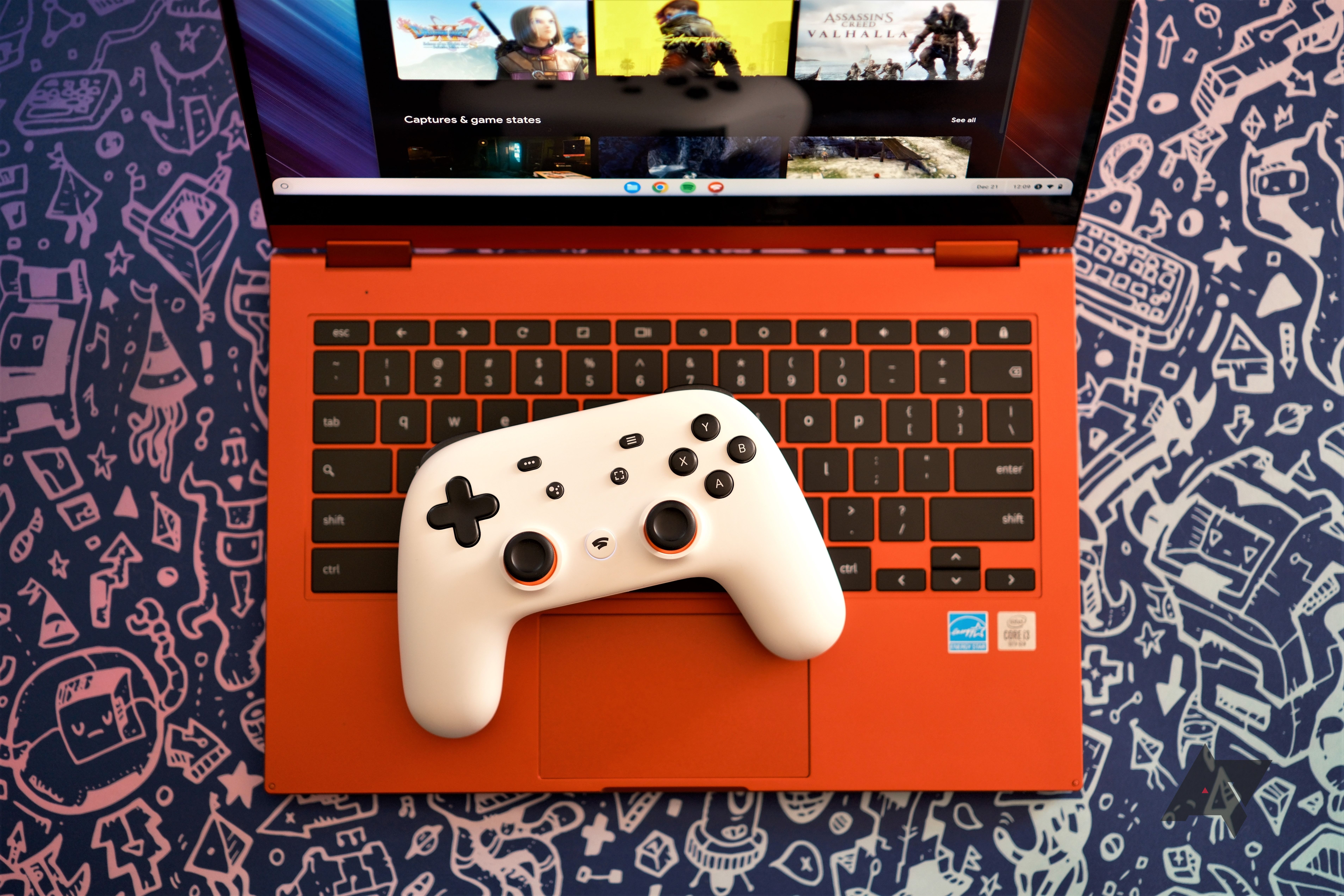 A white Google Stadia controller sitting on the keyboard of a red Chromebook with a gaming service open on the screen. The laptop is sitting on a blue background with silver graphics of video game images.