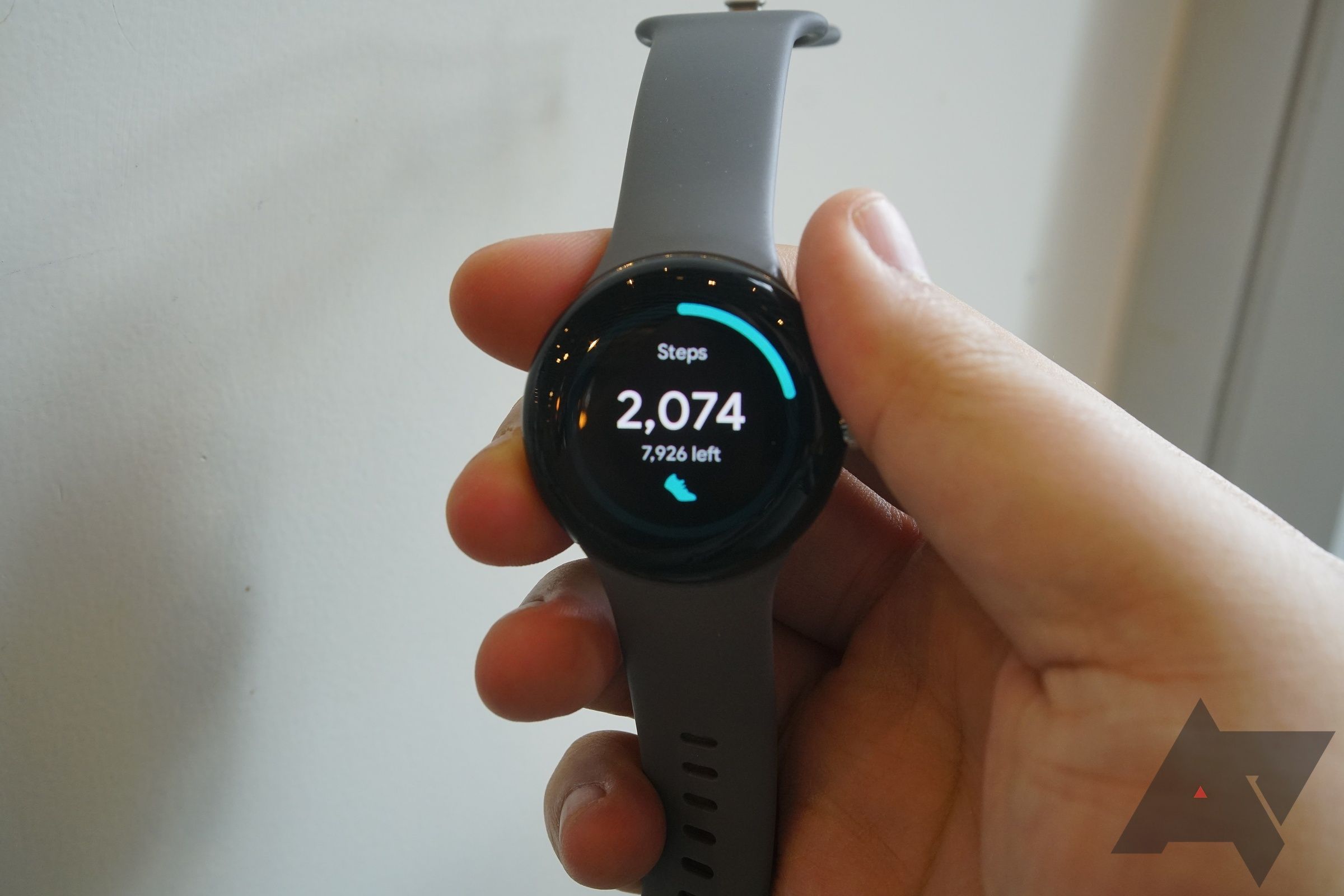 Uma mão segurando um Google Pixel Watch mostrando os passos dados pelo usuário