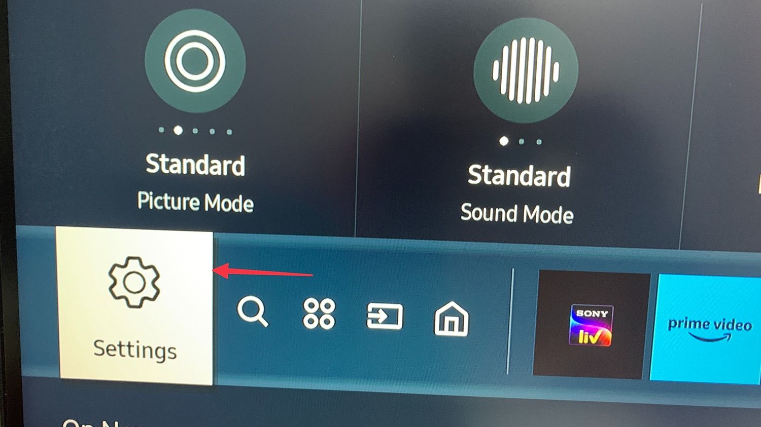 Samsung TV home screen with an arrow pointing to the Settings icon