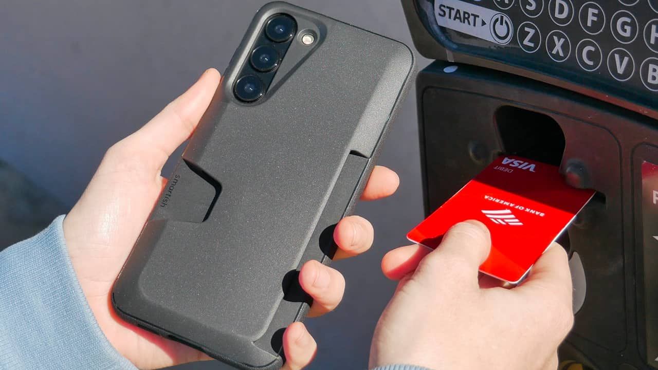 Orang yang memegang Galaxy S23 dalam kasing Smartish Wallet Slayer sambil memasukkan kartu ke dalam mesin bank.